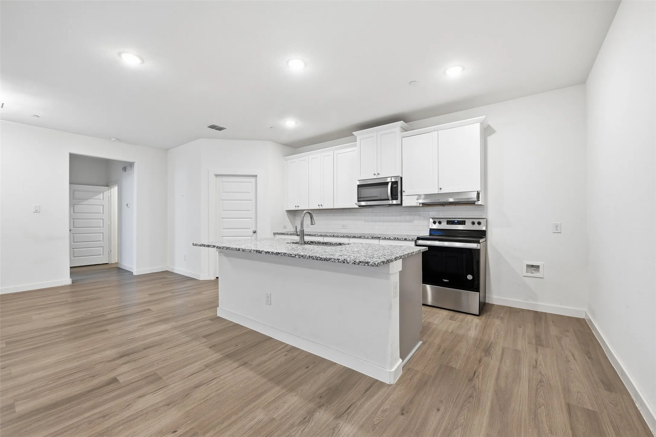 Kitchen with stainless steel appliances, white cabinets, tasteful backsplash, light stone counters, and an island with sink