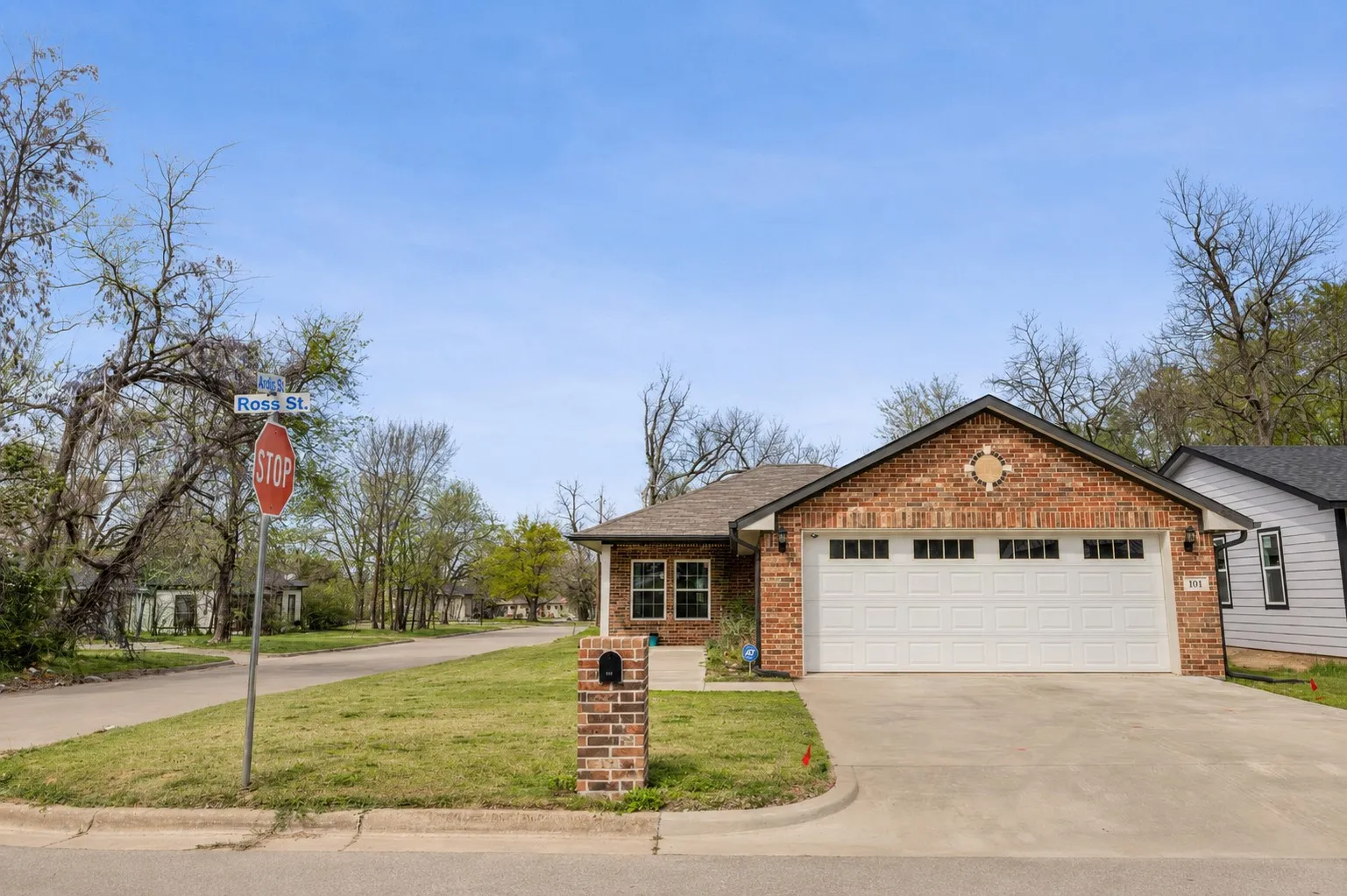 Brick facade home featuring a gable roof, an attached two-car garage with transom windows, a concrete driveway, and a manicured front lawn