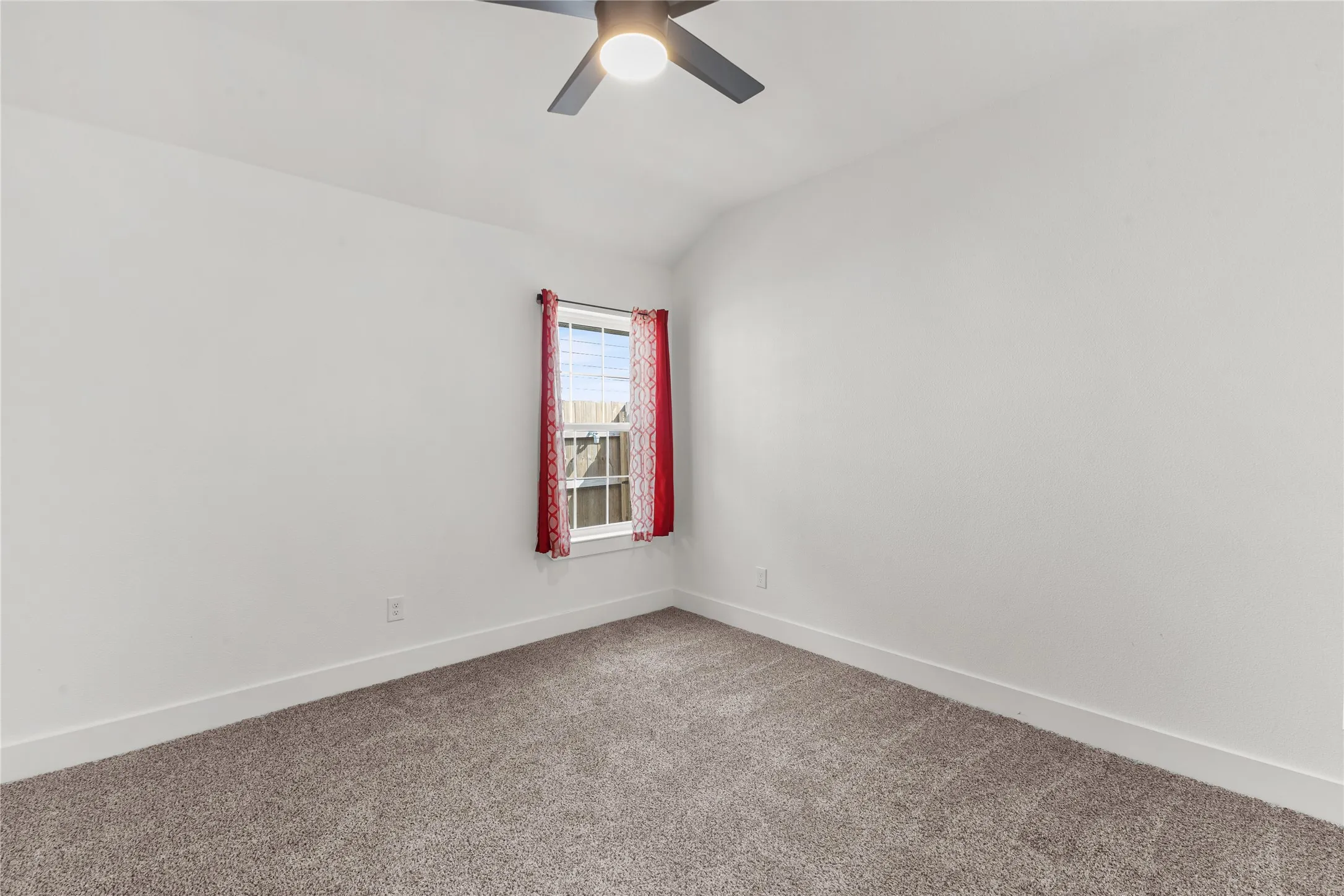 Carpeted spare room featuring lofted ceiling and a ceiling fan
