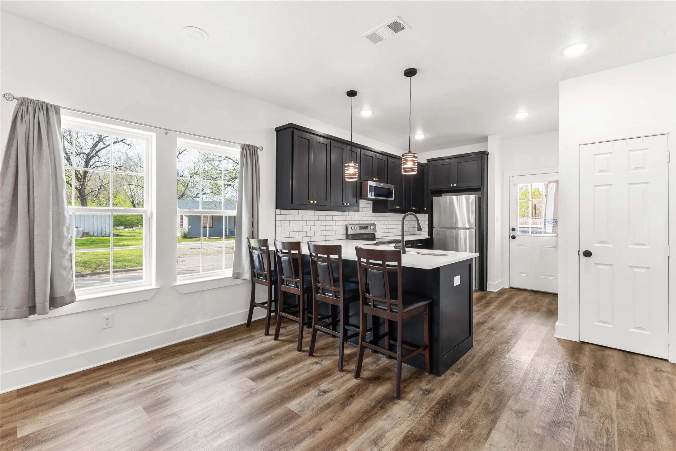 Kitchen with dark cabinetry, a peninsula, a breakfast bar area, hanging light fixtures, and dark wood-style floors