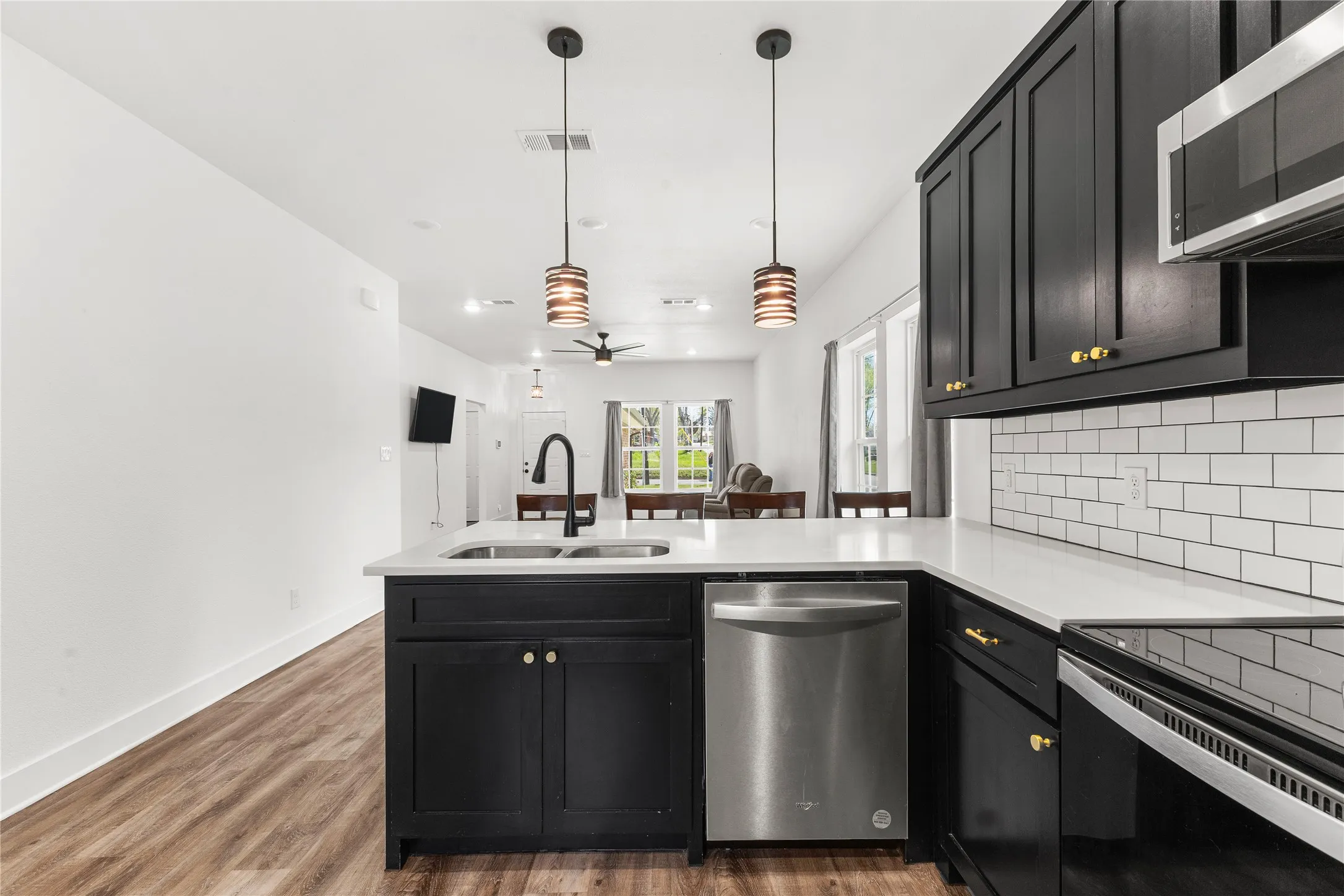 Kitchen with dark cabinets, stainless steel appliances, decorative light fixtures, a peninsula, and decorative backsplash