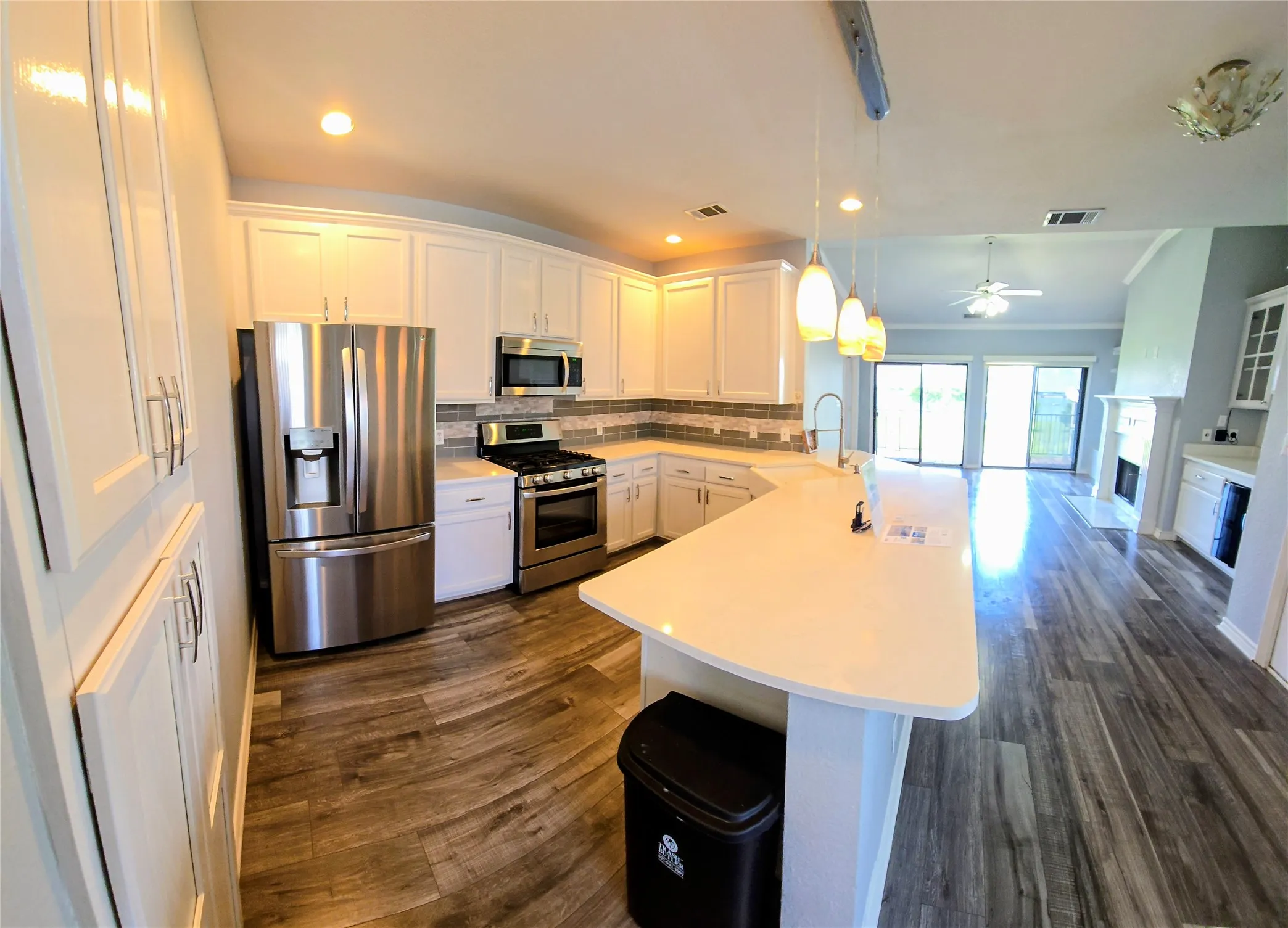 Kitchen featuring white cabinetry, stainless steel appliances, a curved peninsula with pendant lighting, and wood-finish flooring