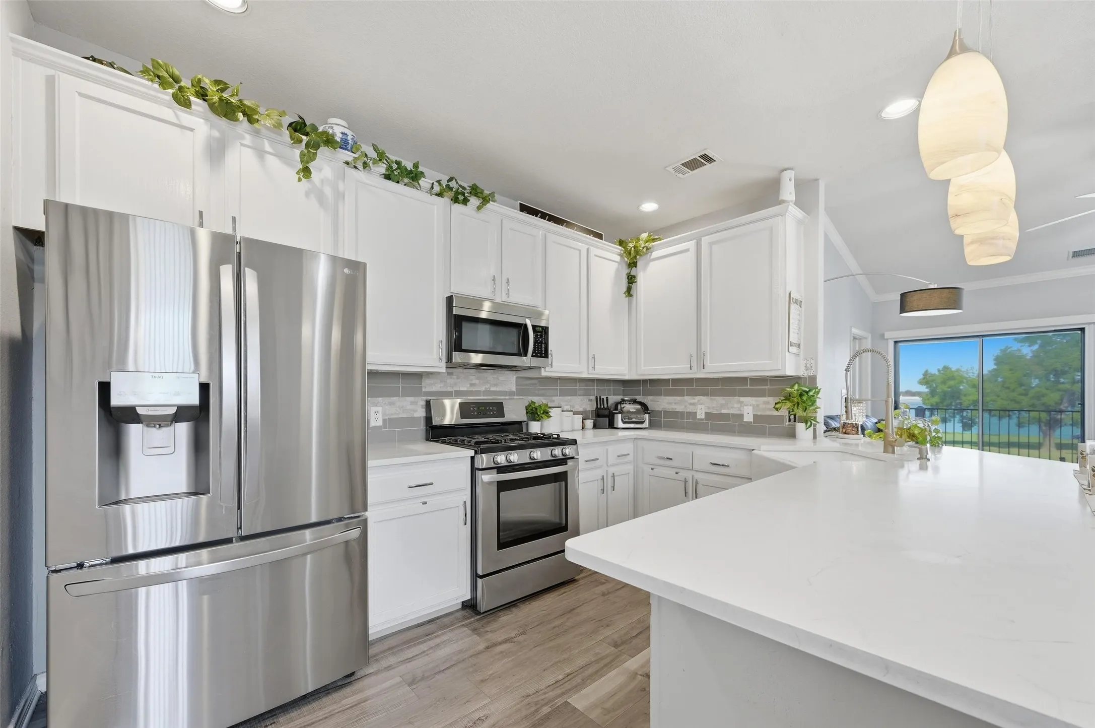 Kitchen featuring appliances with stainless steel finishes, white cabinets, tasteful backsplash, decorative light fixtures, and light wood-style floors