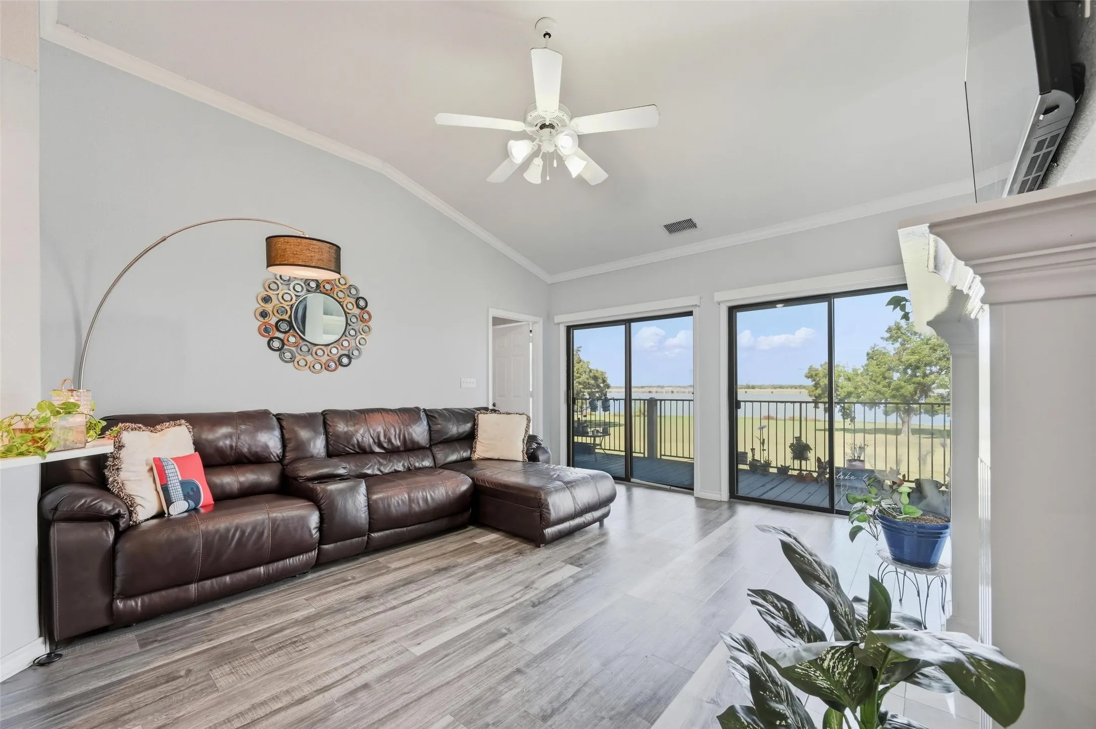 Living area with vaulted ceiling, ornamental molding, wood finished floors, ceiling fan, and a water view