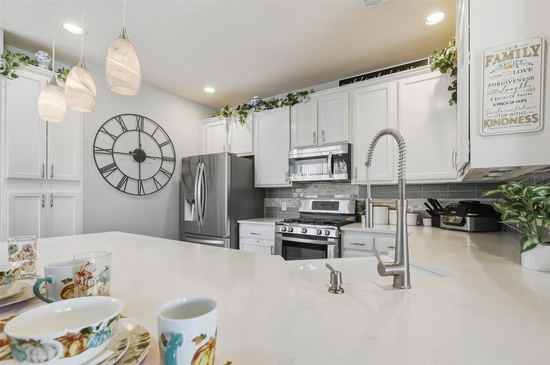 Kitchen featuring white cabinets, appliances with stainless steel finishes, decorative backsplash, decorative light fixtures, and light stone countertops