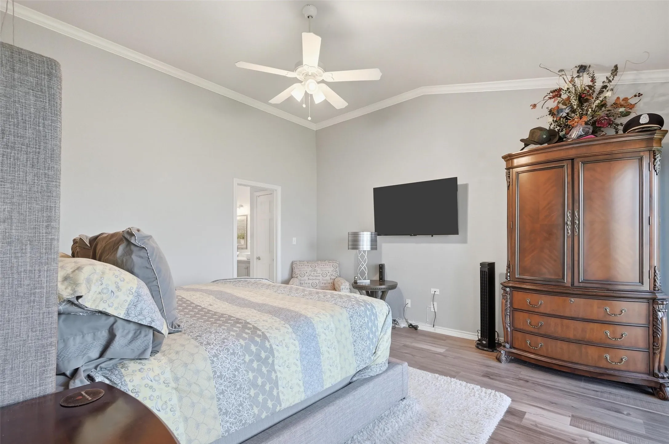 Bedroom with crown molding, light wood-style flooring, lofted ceiling, connected bathroom, and ceiling fan