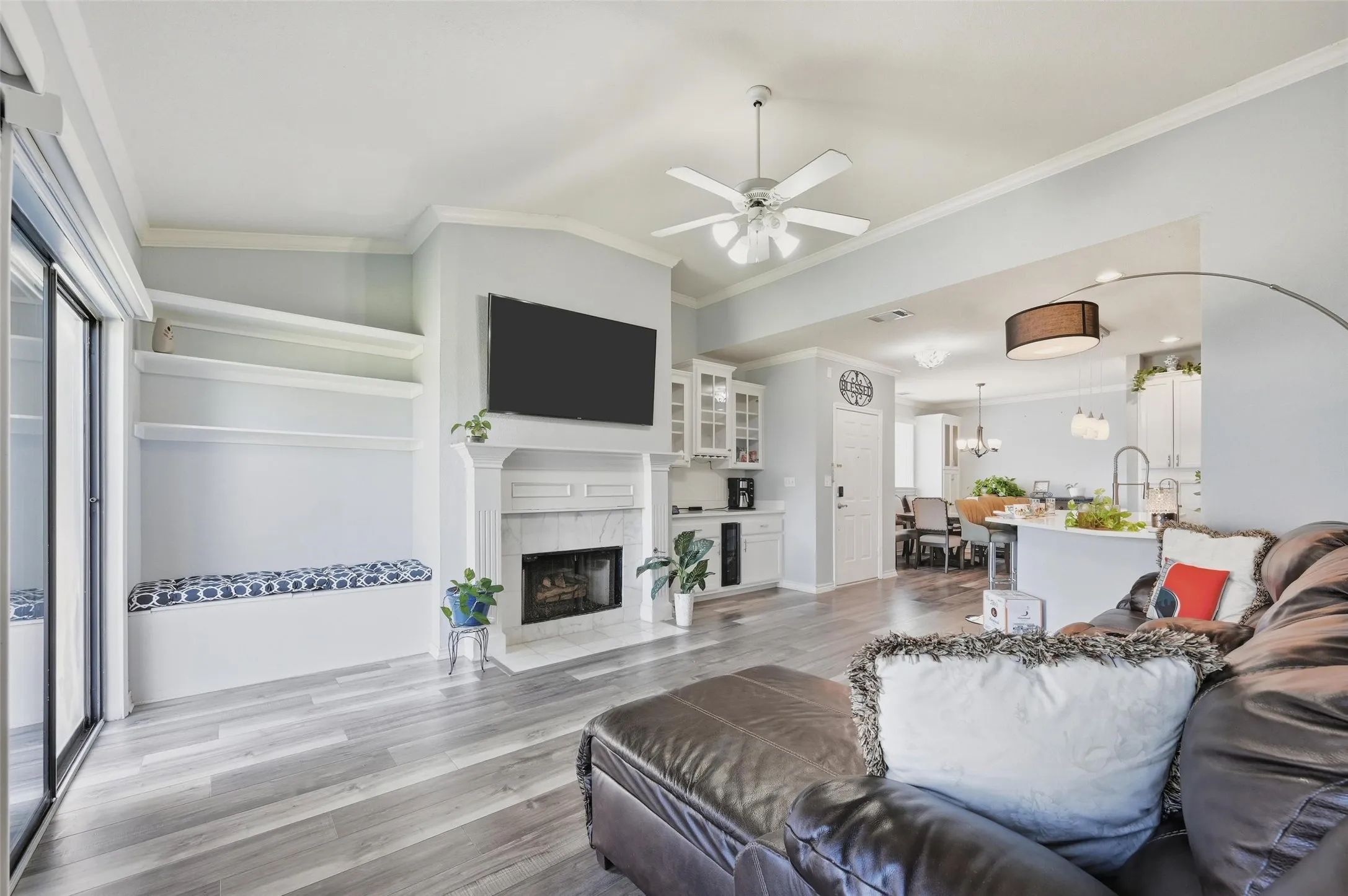 Living area with light wood-type flooring, ornamental molding, ceiling fan, a tiled fireplace, and a chandelier