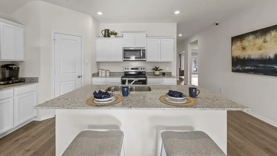 Kitchen featuring white cabinets, stainless steel appliances, light stone countertops, a kitchen bar, and dark wood-style floors