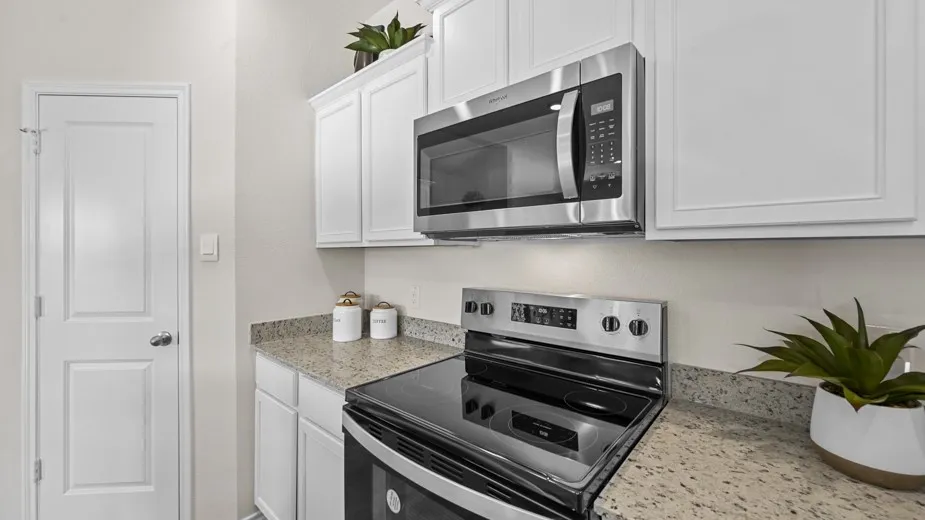 Kitchen with stainless steel appliances, white cabinetry, and light stone counters
