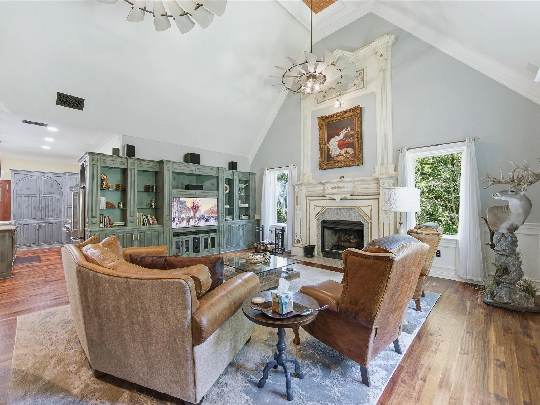Vaulted ceiling living area featuring a prominent fireplace with an ornate mantel, a full-wall built-in media center with open shelving, wood-finish flooring, and large windows