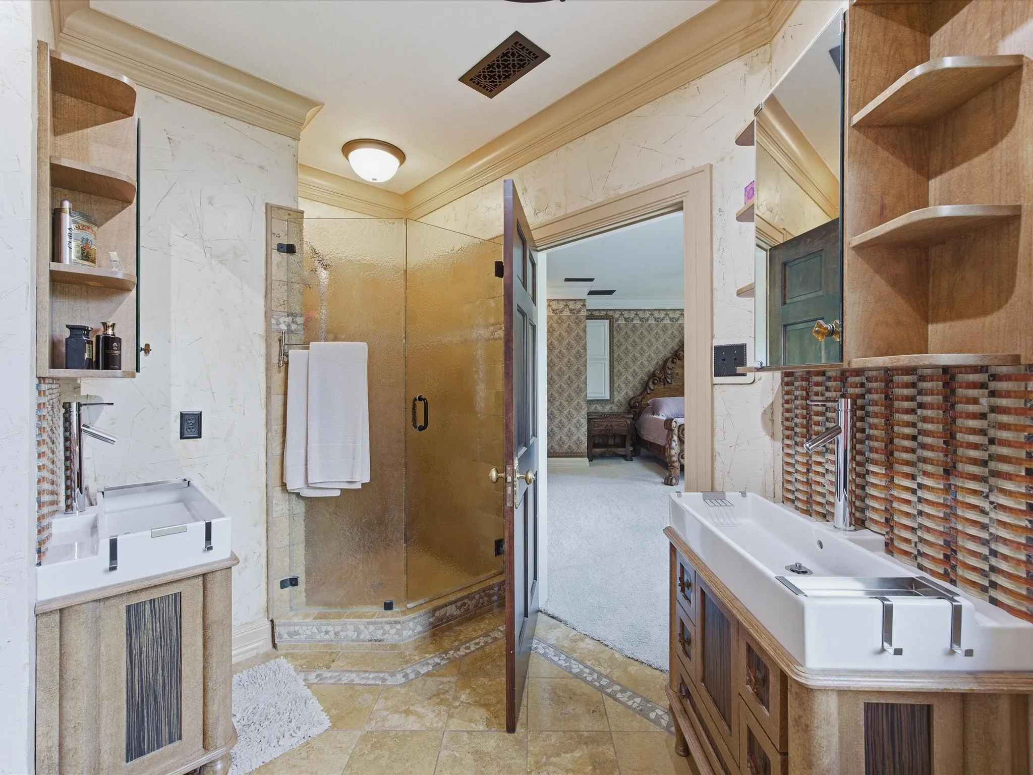 Bathroom featuring dual custom wood-finish vanities with vessel sinks, a glass-enclosed shower, and patterned tile flooring