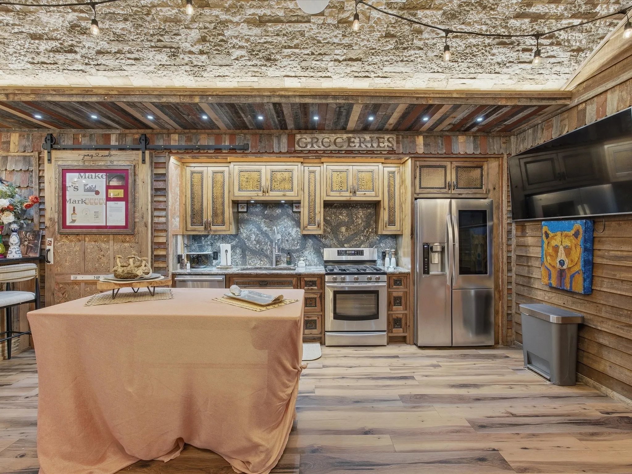 Kitchen featuring a stainless steel French door refrigerator, stainless steel gas range, stone countertops, wood-finish flooring, and a barn door entry