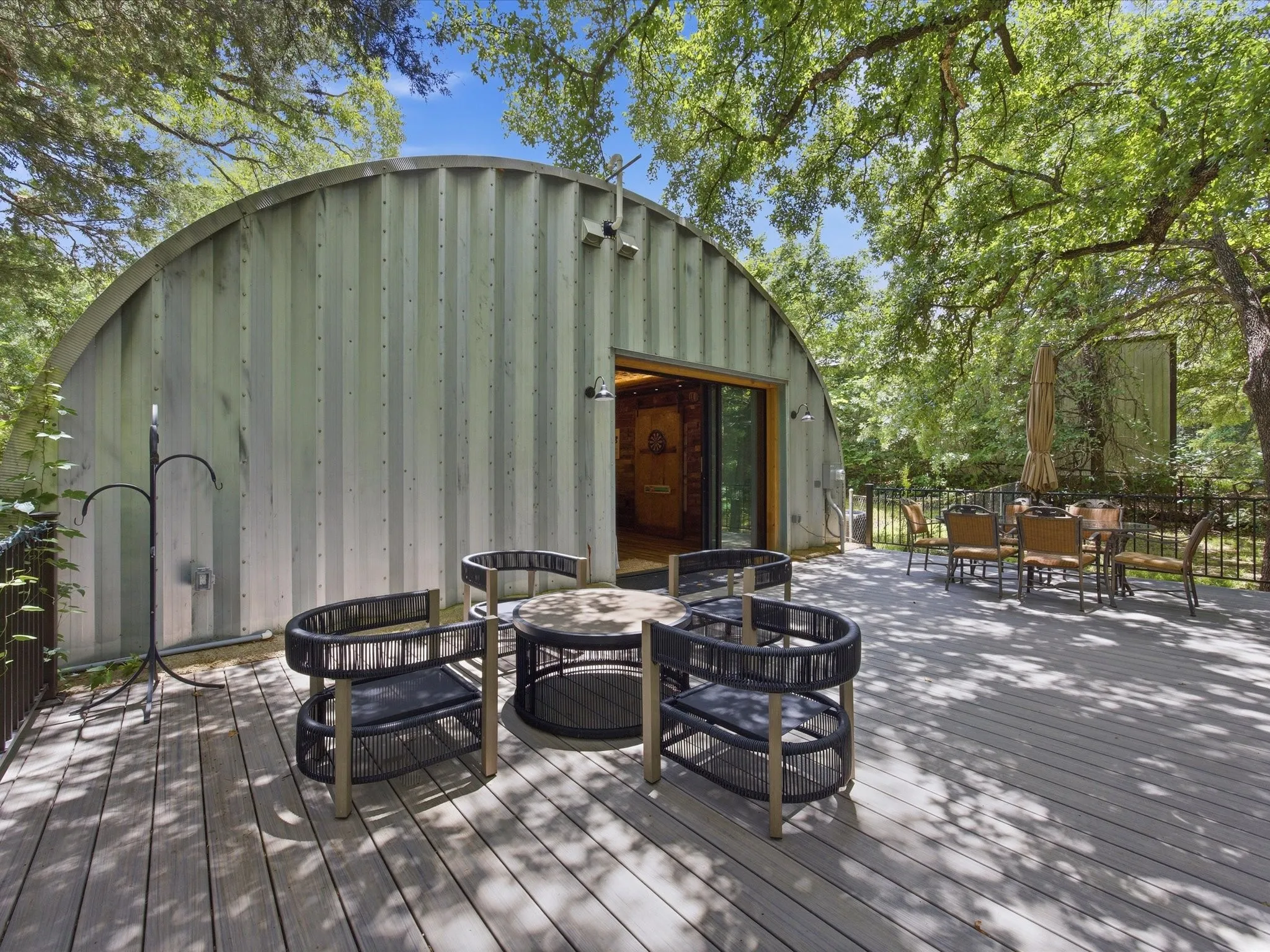 Exterior with a curved metal facade, expansive wood-finish deck, sliding glass door, and abundant mature trees
