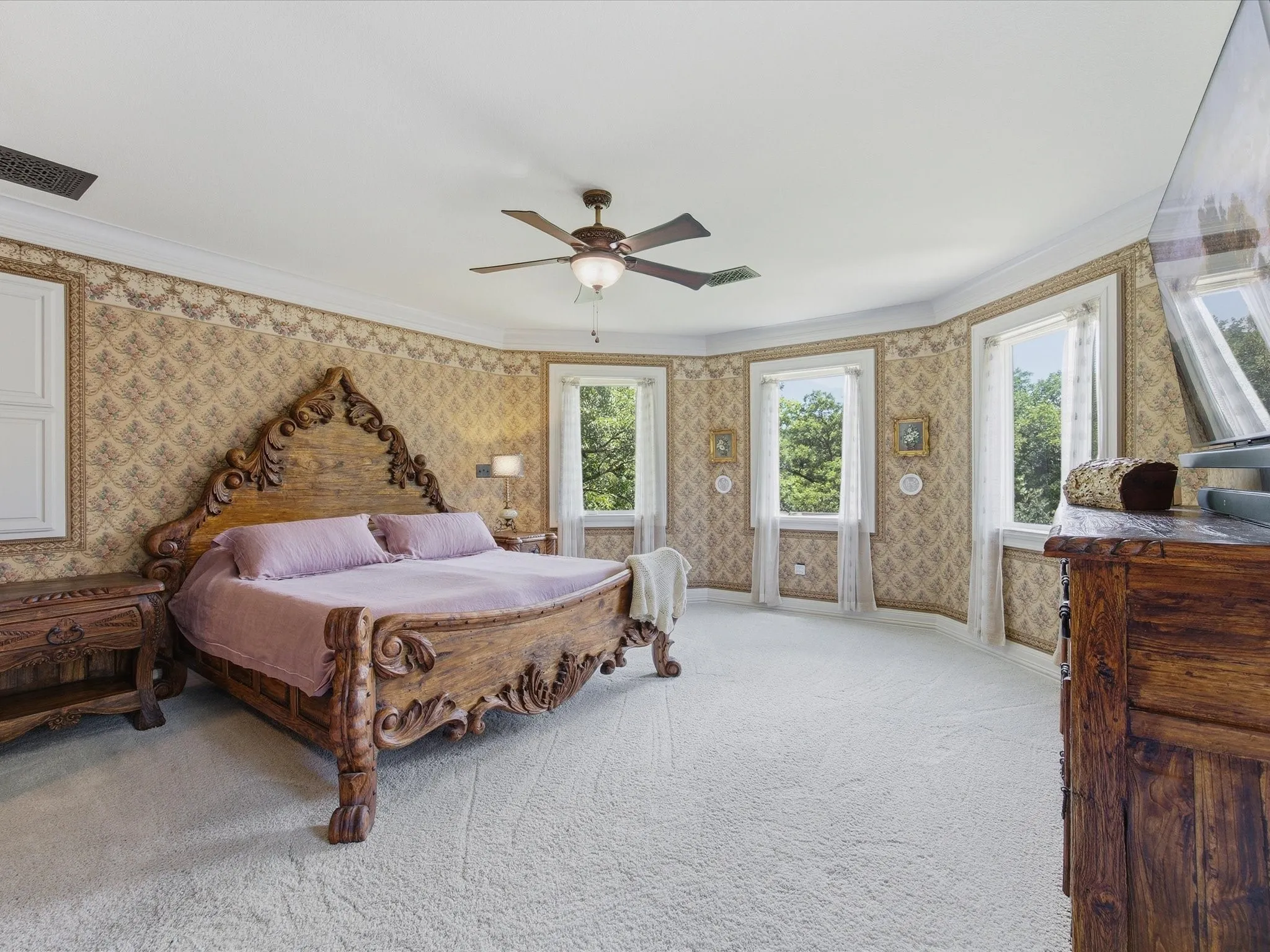 Spacious bedroom featuring patterned wallpaper, crisp white crown molding, a ceiling fan, and multiple windows