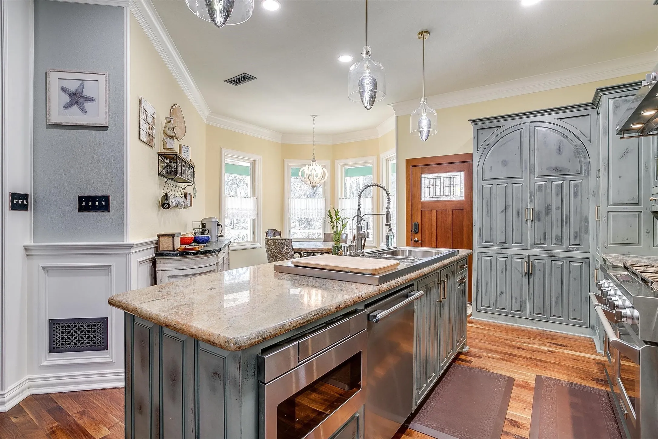 Kitchen featuring stainless steel appliances, an island with sink, light stone countertops, ornamental molding, and suspended lighting