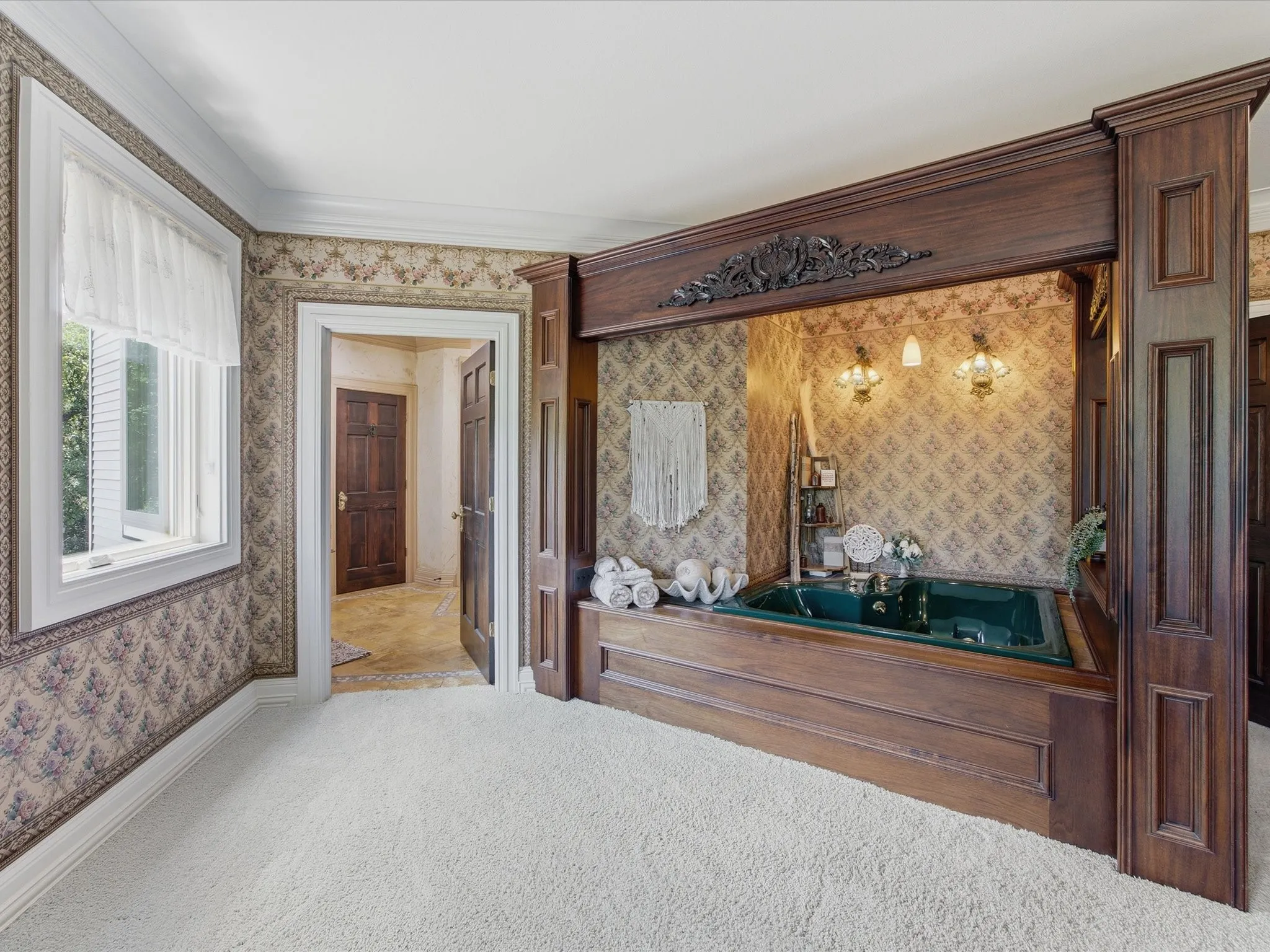 Recessed soaking tub set within a dark wood surround, featuring ornate carved details, and flanked by wall-mounted sconces