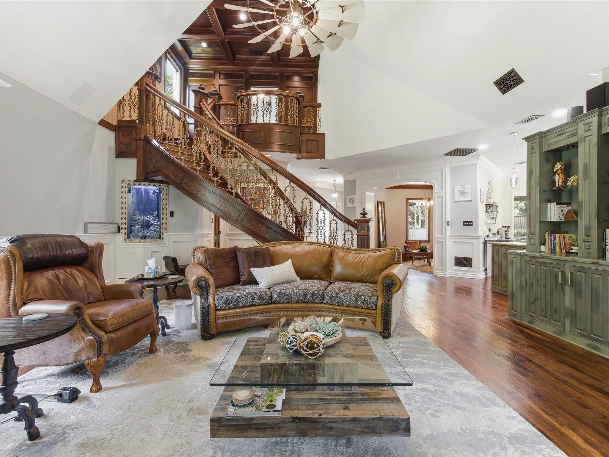 Grand open-concept living space with a multi-level wood staircase featuring ornate metal railings and a built-in balcony