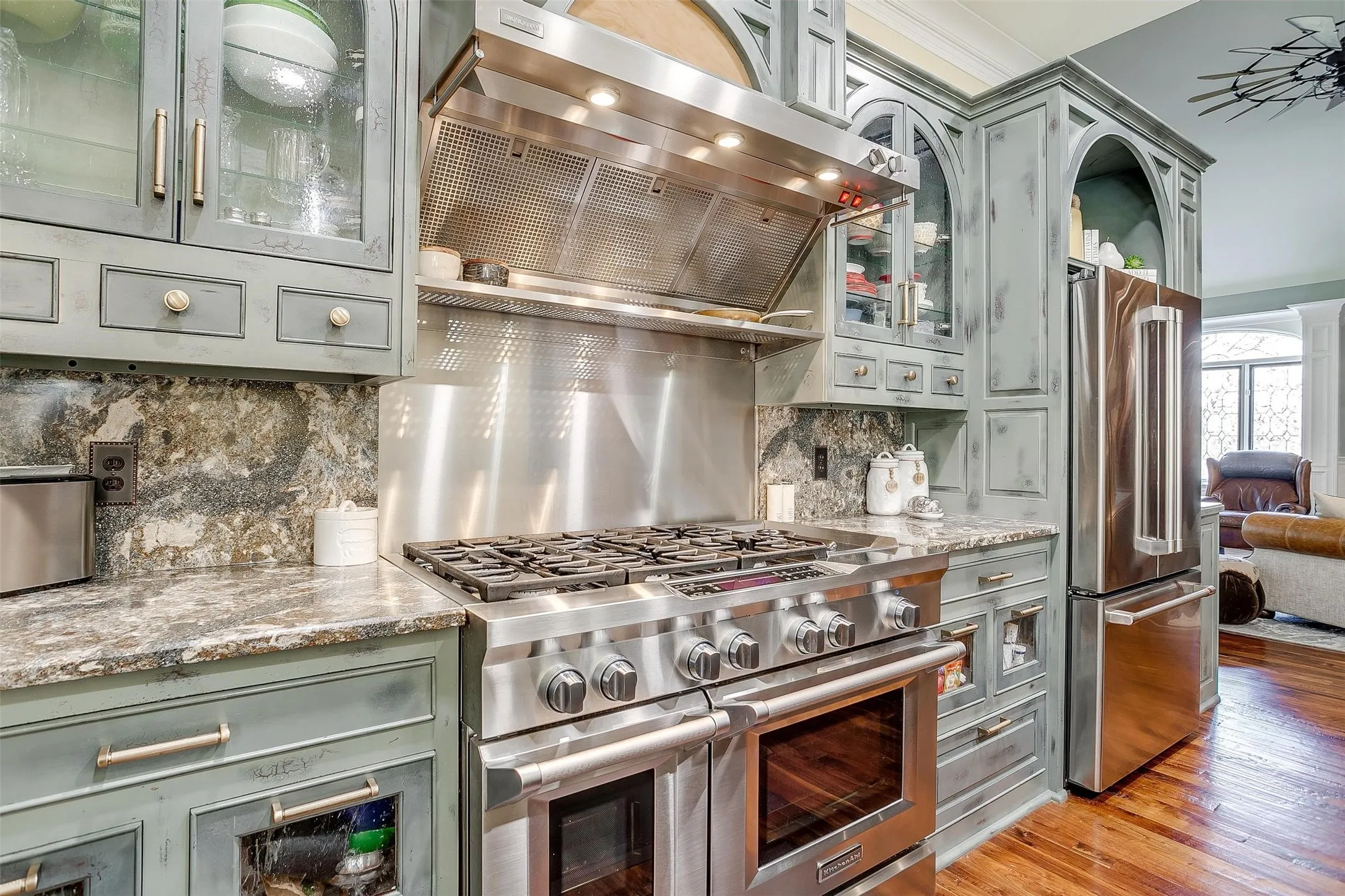 Kitchen with glass fronted cabinets, high end appliances, ventilation hood, light stone counters, and crown molding