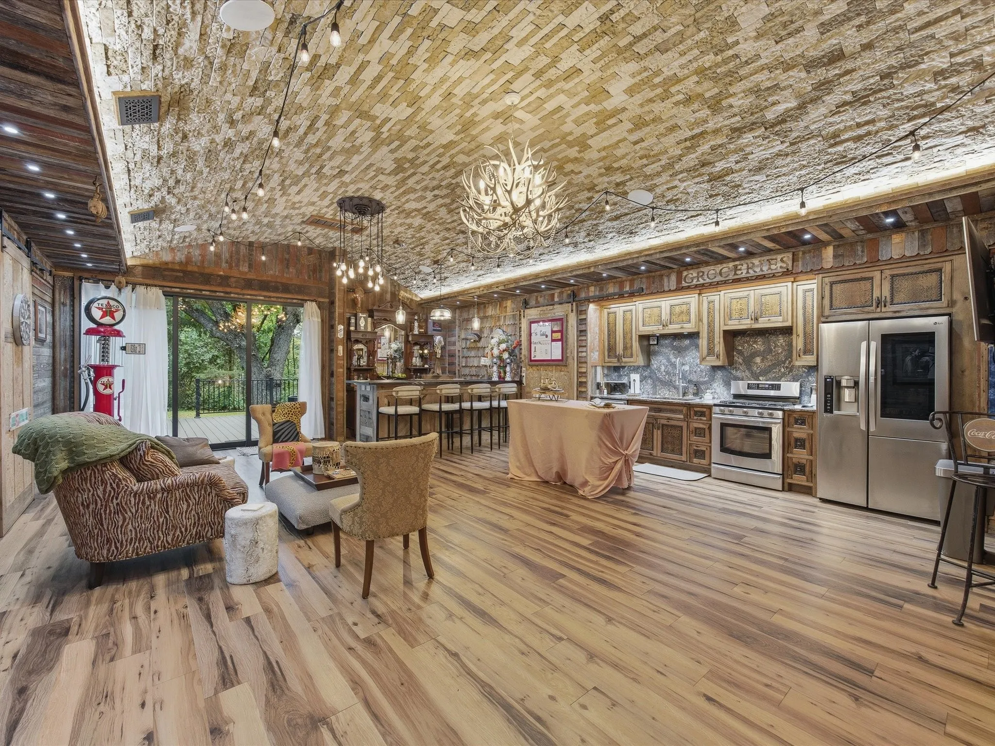 Spacious open-concept living area featuring wood-finish flooring, wood paneling, and a brick-patterned ceiling with recessed and string lighting