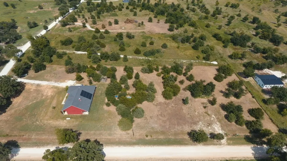 Expansive rural property featuring a red single-story residence with a dark shingled roof and solar panels