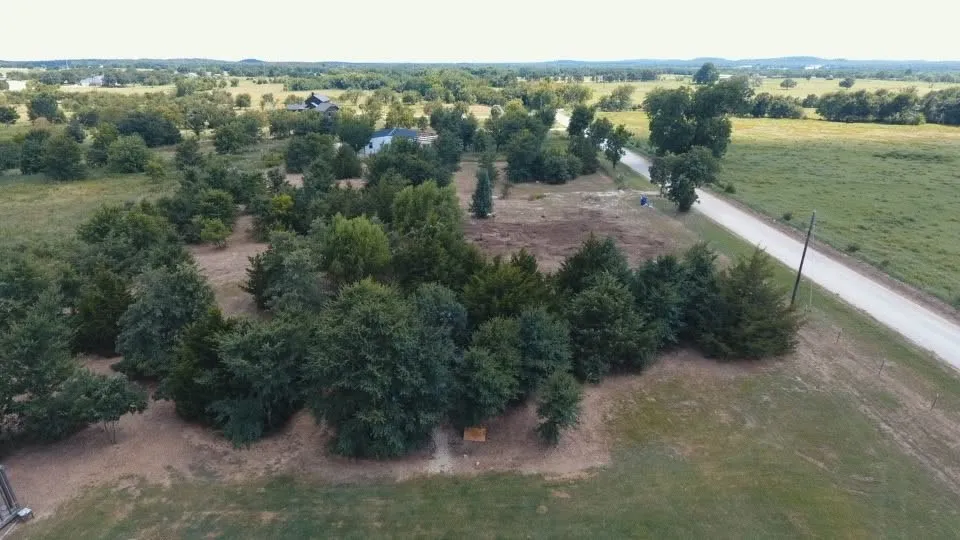 Expansive land parcel featuring a gravel road, abundant mature trees, and a distant structure