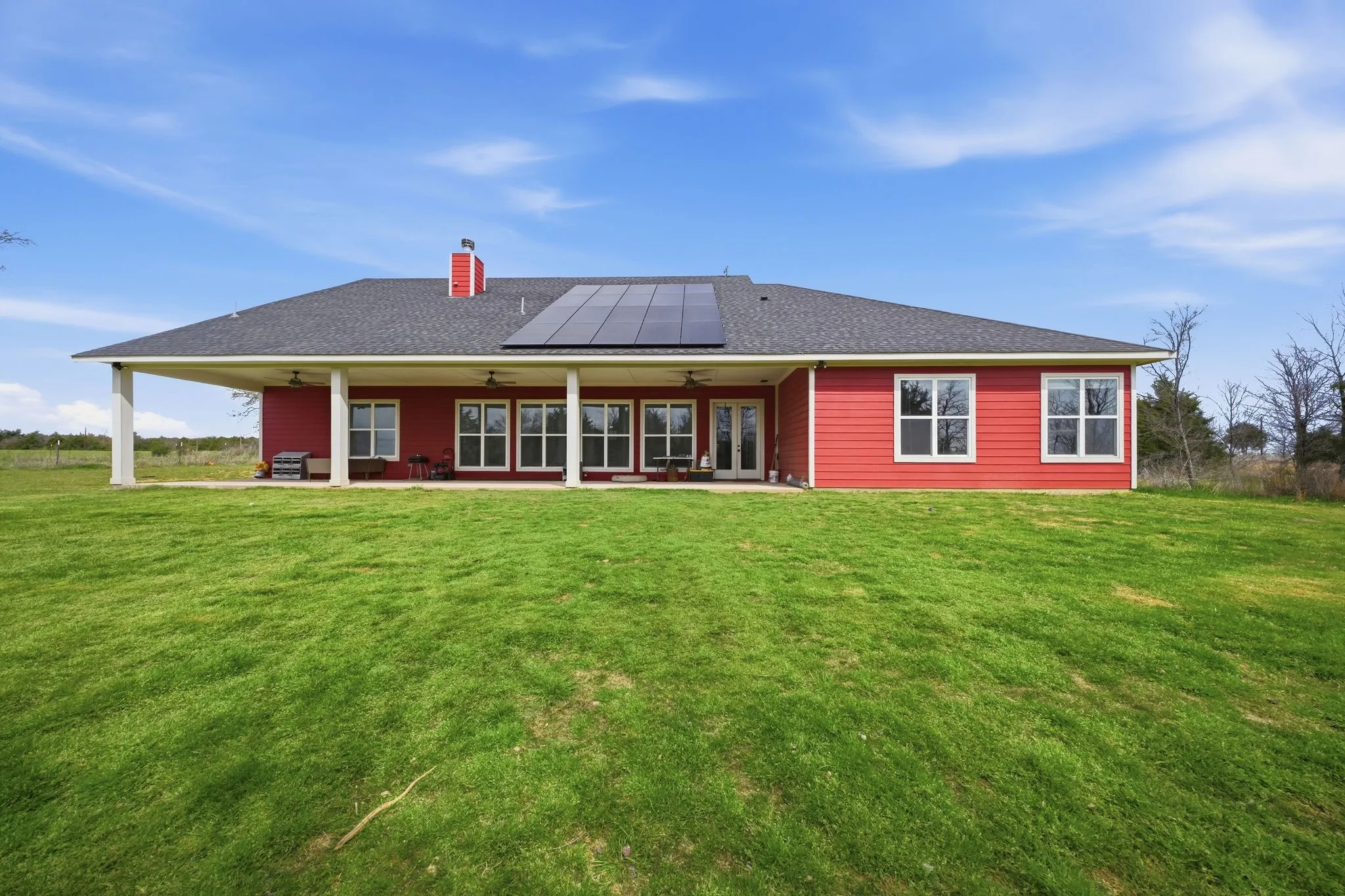 Back of property featuring ceiling fan, roof mounted solar panels, a patio area, a lawn, and a chimney