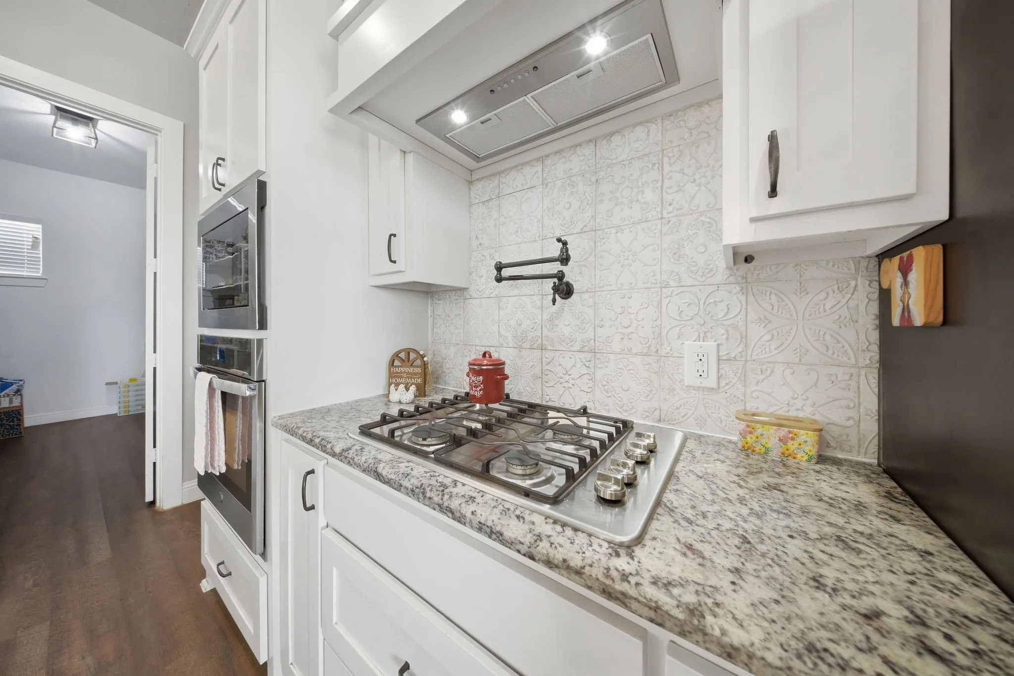 Kitchen with exhaust hood, white cabinetry, light stone counters, and stainless steel appliances