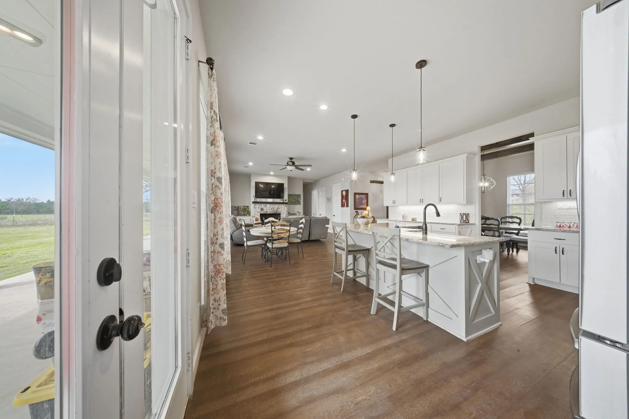 Kitchen featuring open floor plan, a stone fireplace, freestanding refrigerator, dark wood-type flooring, and white cabinetry