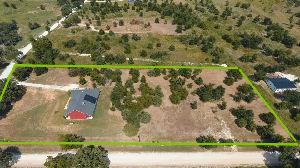 Expansive rural property featuring a single-story red-sided residence with a dark roof and solar panels