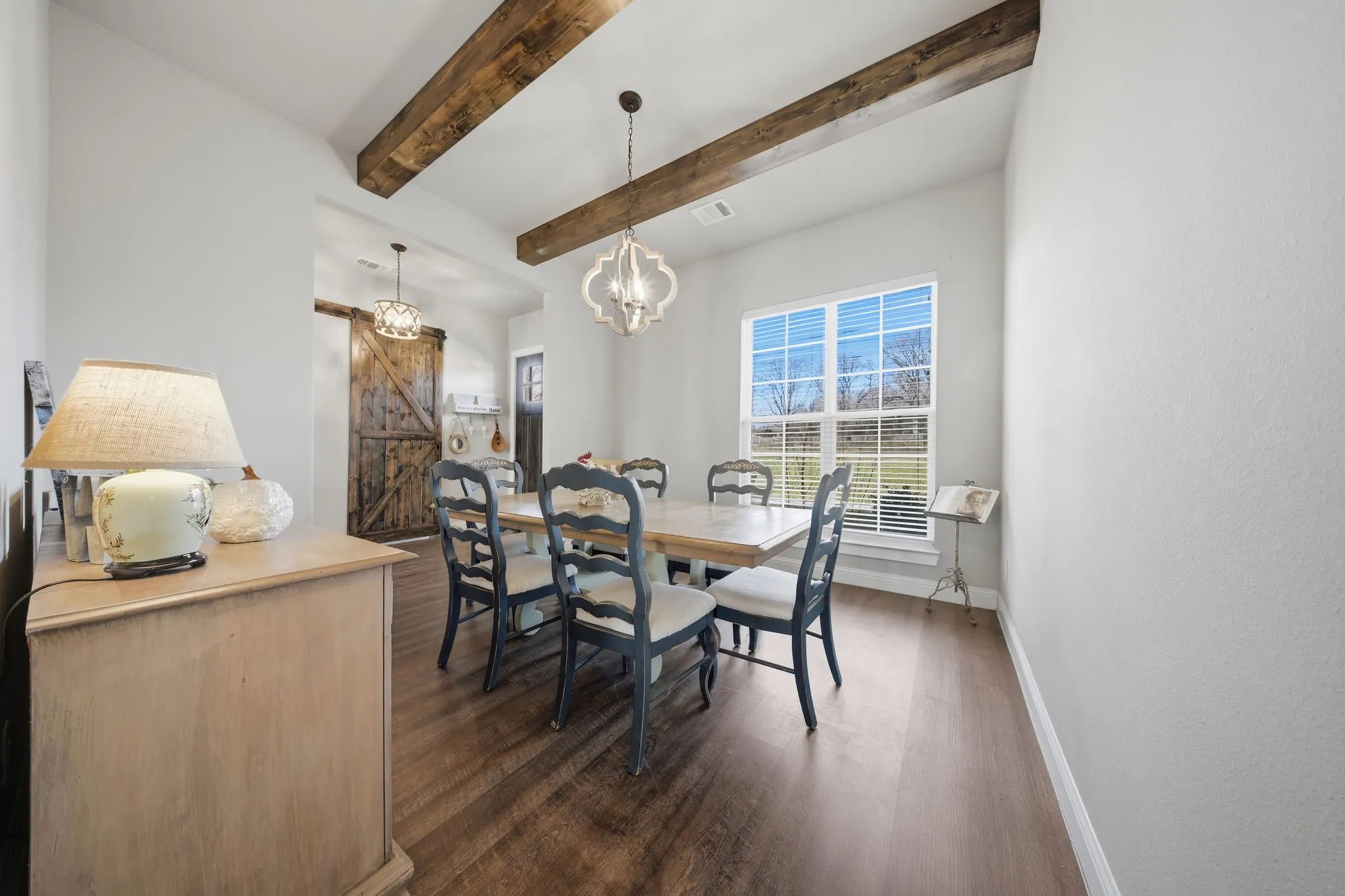Dining area featuring a barn door, dark wood-type flooring, beam ceiling, and a chandelier