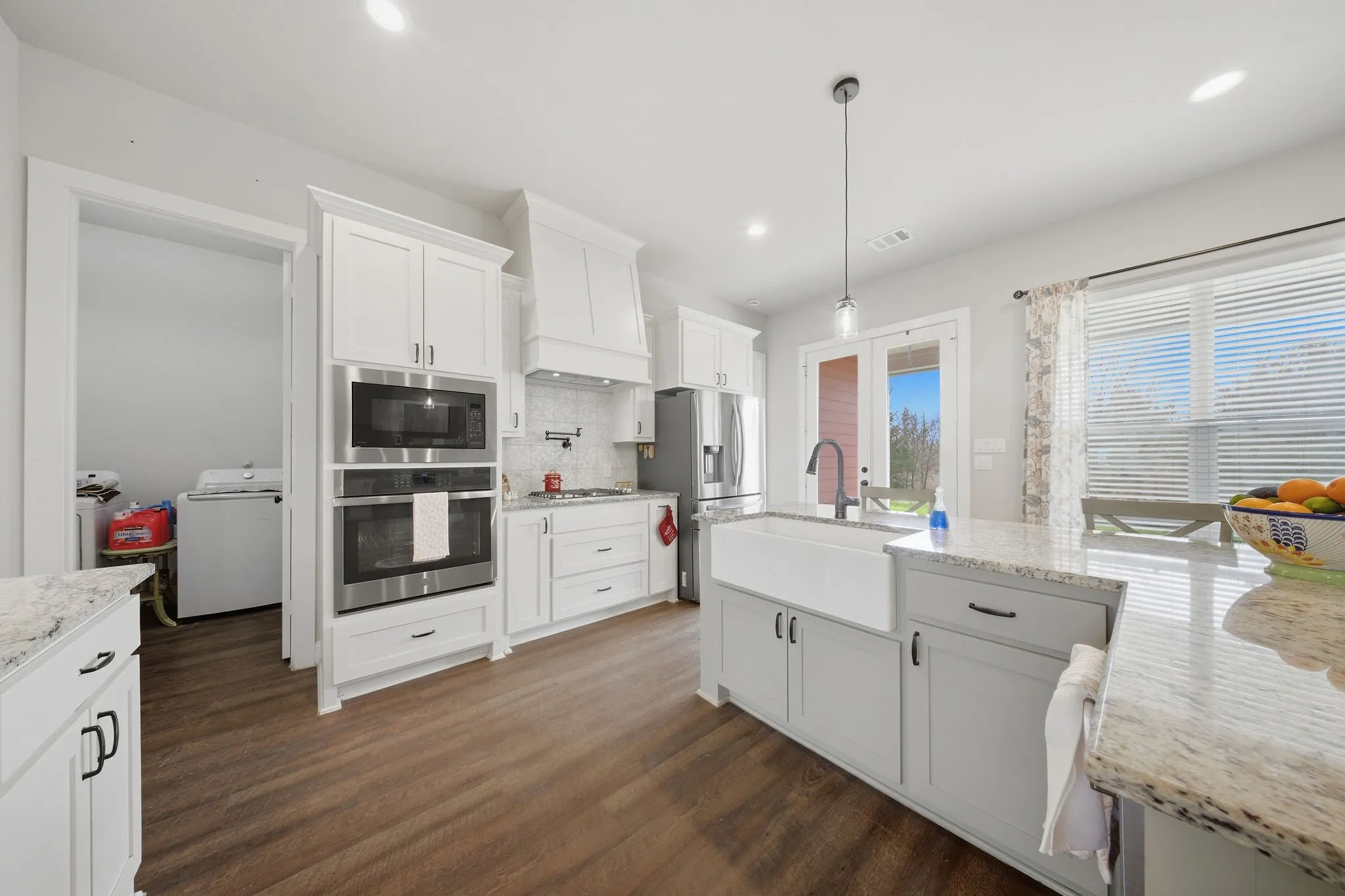 Kitchen with stainless steel appliances, dark wood-style flooring, white cabinets, and light stone counters
