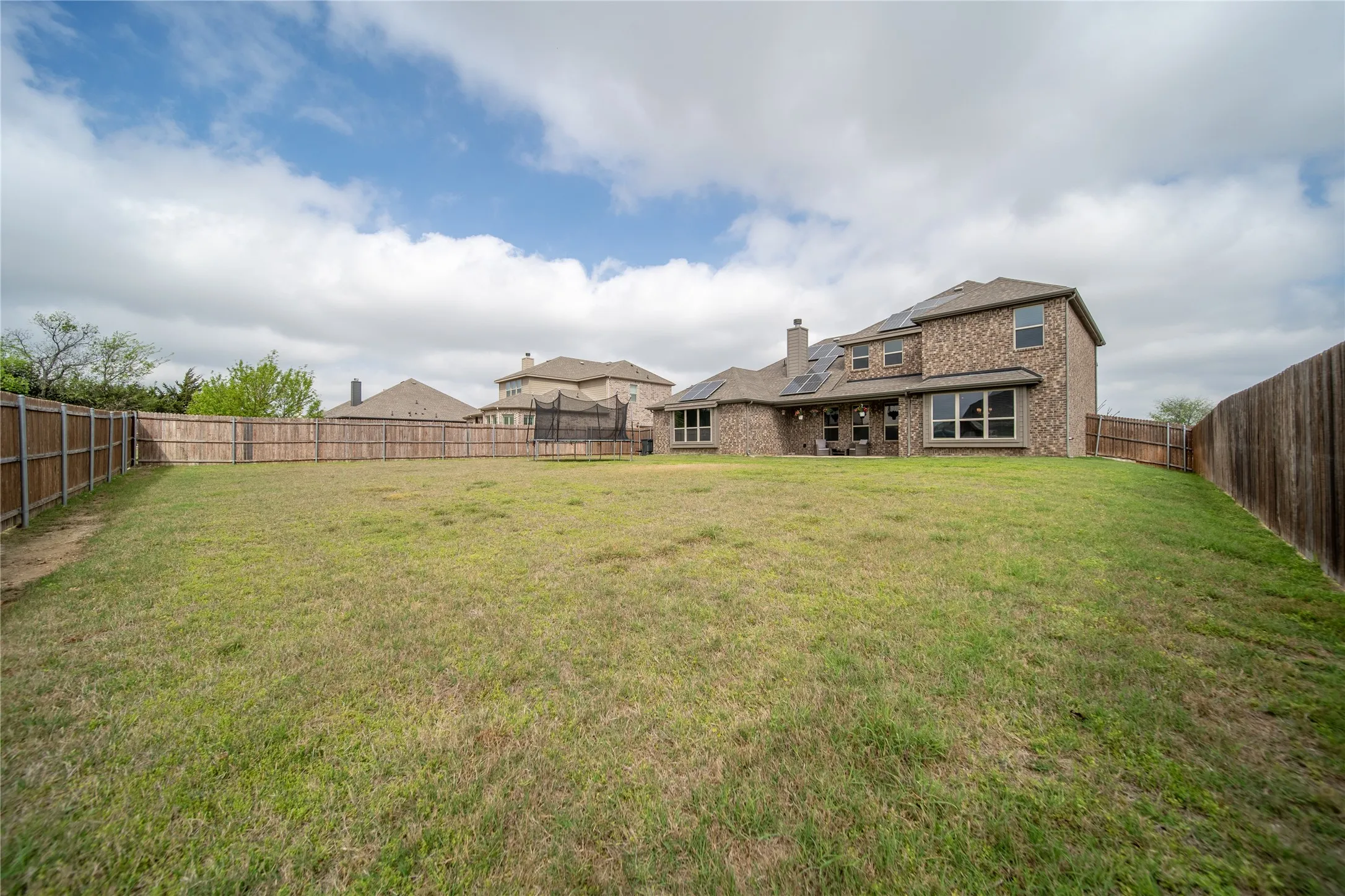 Rear view of house with a fenced backyard, brick siding, a chimney, a patio area, and a trampoline