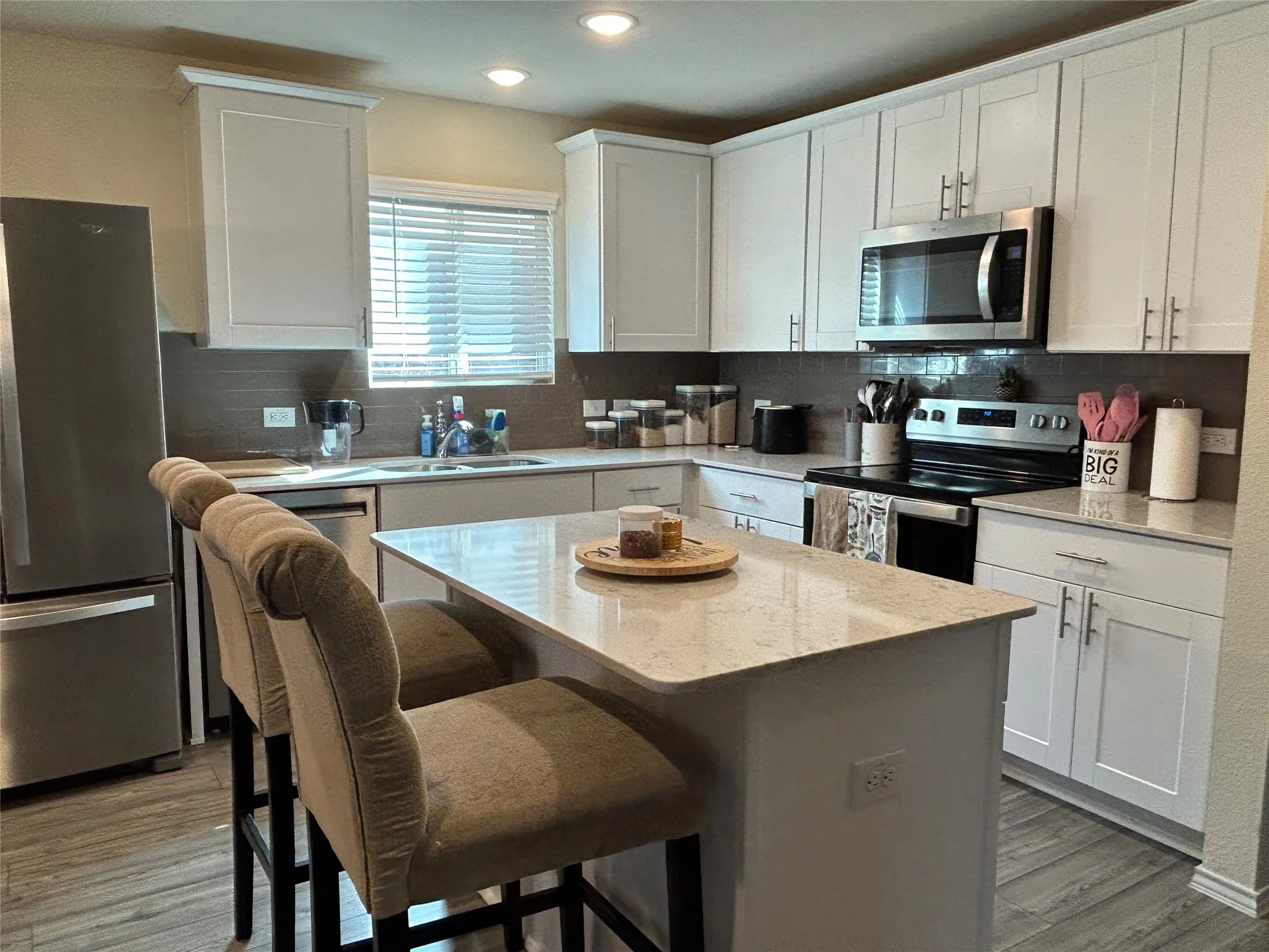 Kitchen with stainless steel appliances, white cabinets, a kitchen breakfast bar, light stone counters, and a kitchen island