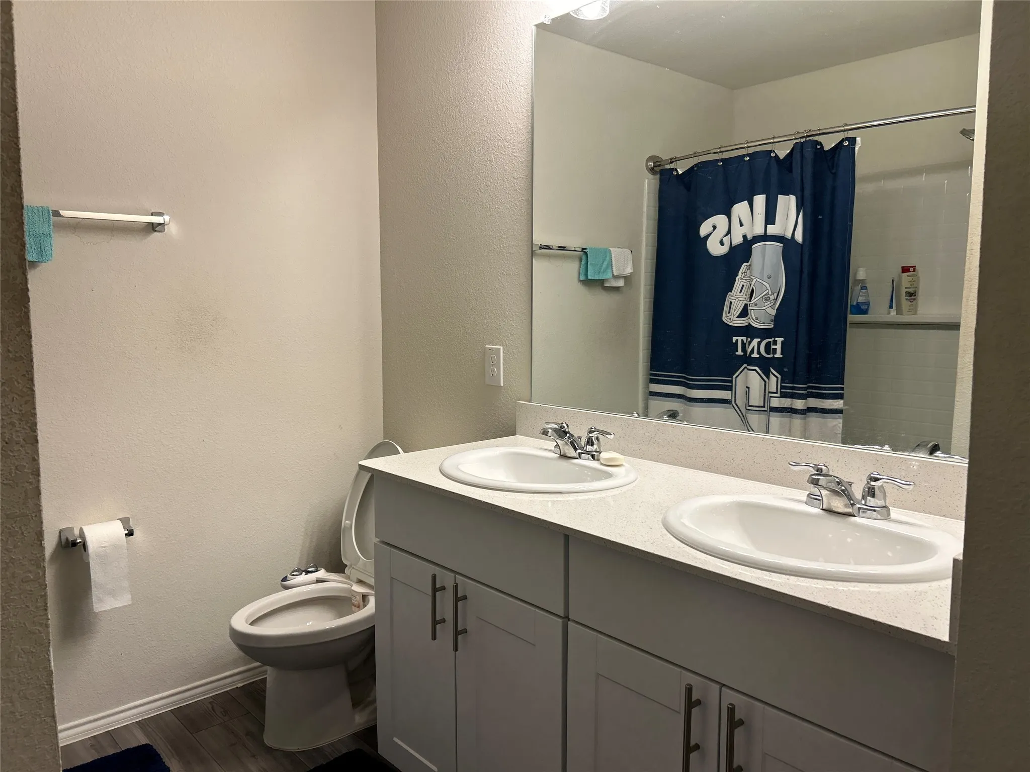 Bathroom featuring a textured wall, double vanity, dark wood finished floors, and a shower with shower curtain