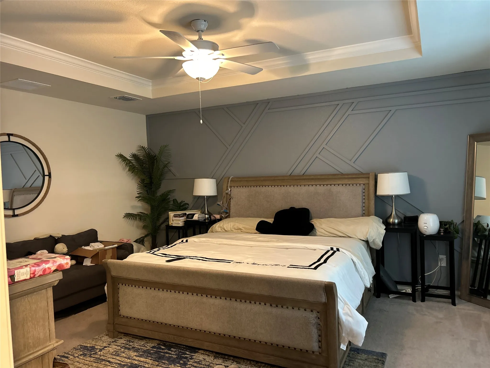 Bedroom with a tray ceiling, carpet flooring, crown molding, ceiling fan, and a decorative wall