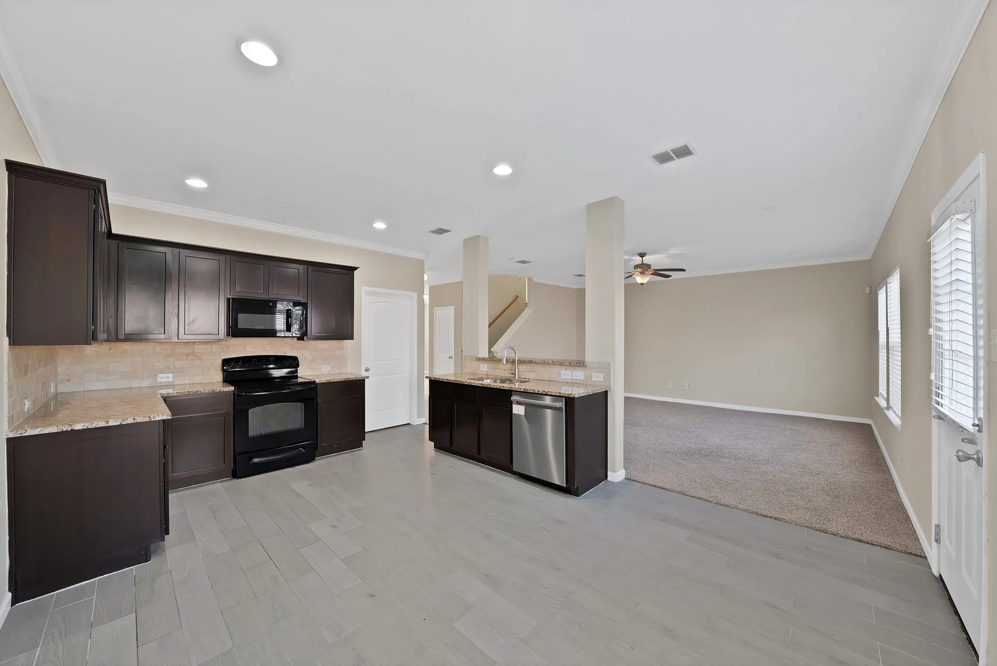 Kitchen featuring black appliances, ornamental molding, open floor plan, light stone countertops, and dark wood finish cabinets