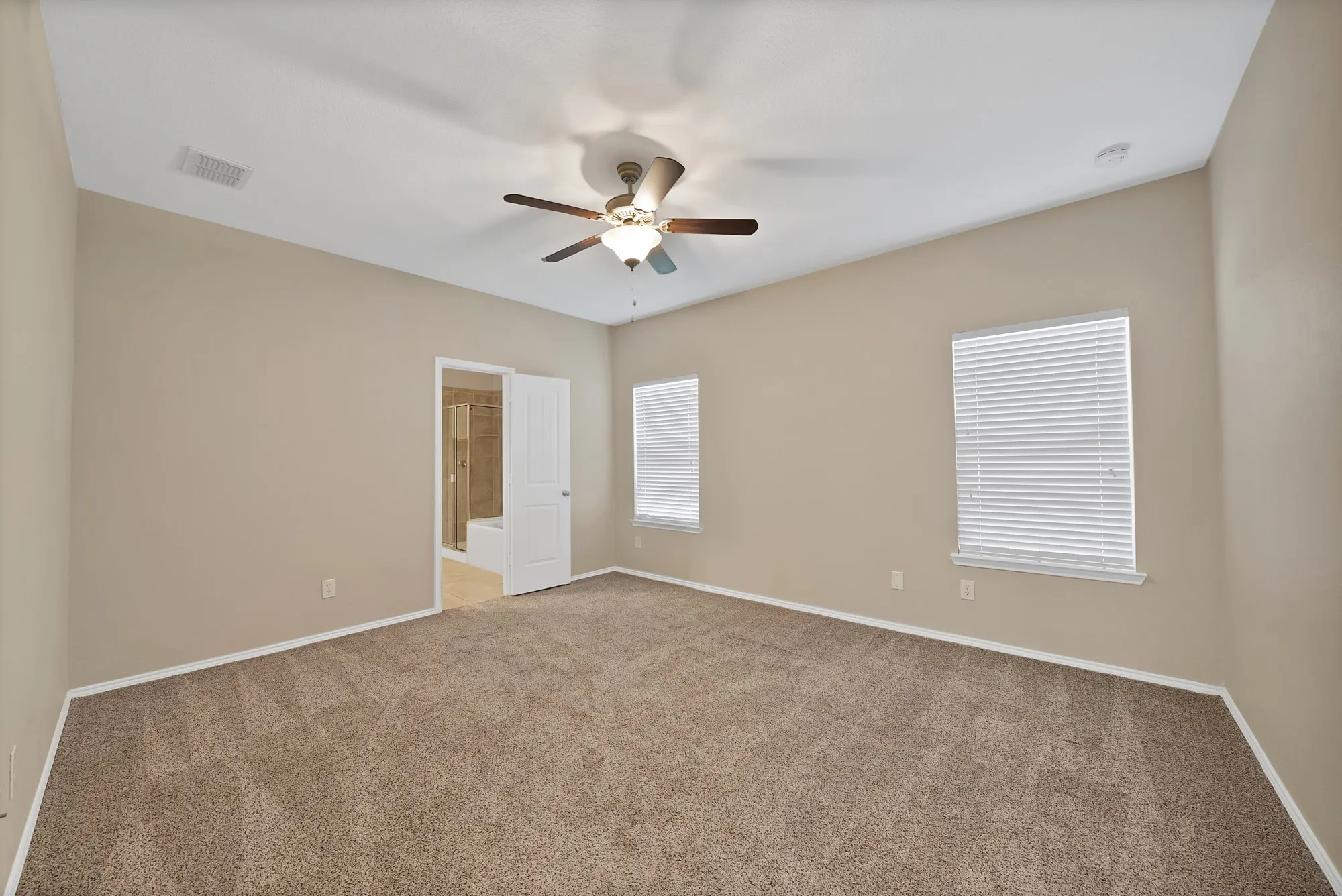 Unfurnished bedroom with light colored carpet, ceiling fan, and ensuite bath