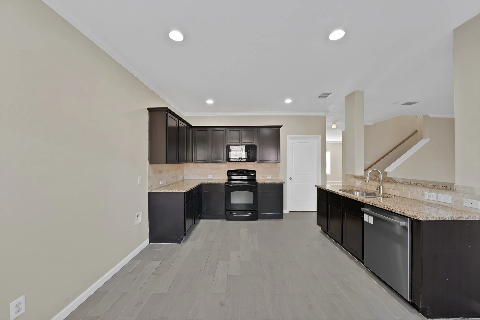 Kitchen featuring black appliances, light stone countertops, decorative backsplash, ornamental molding, and dark wood finish cabinetry