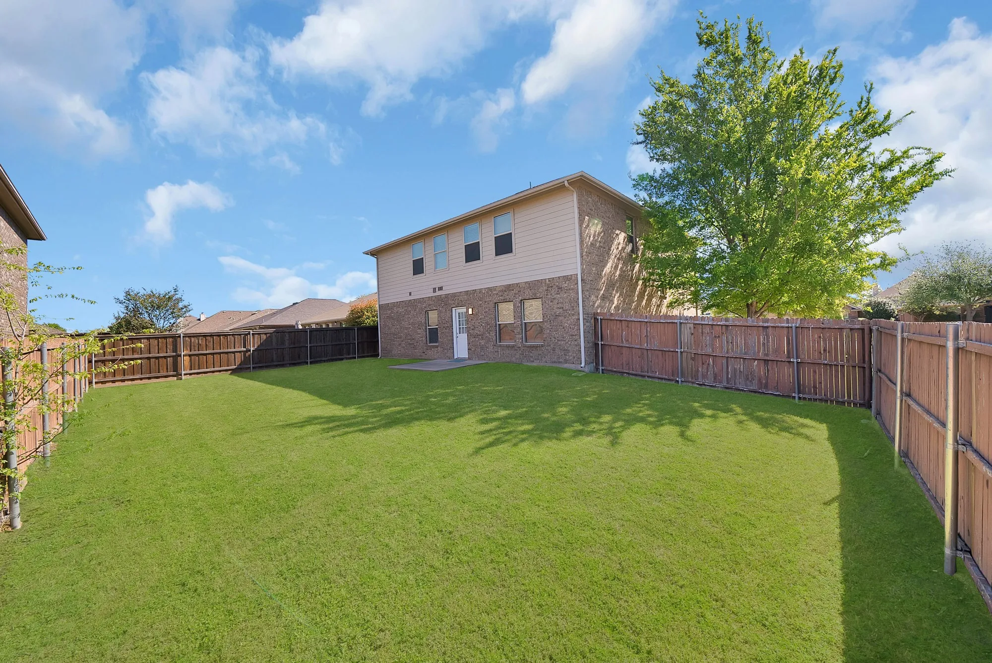 Rear view of house with a fenced backyard, a patio, and brick siding