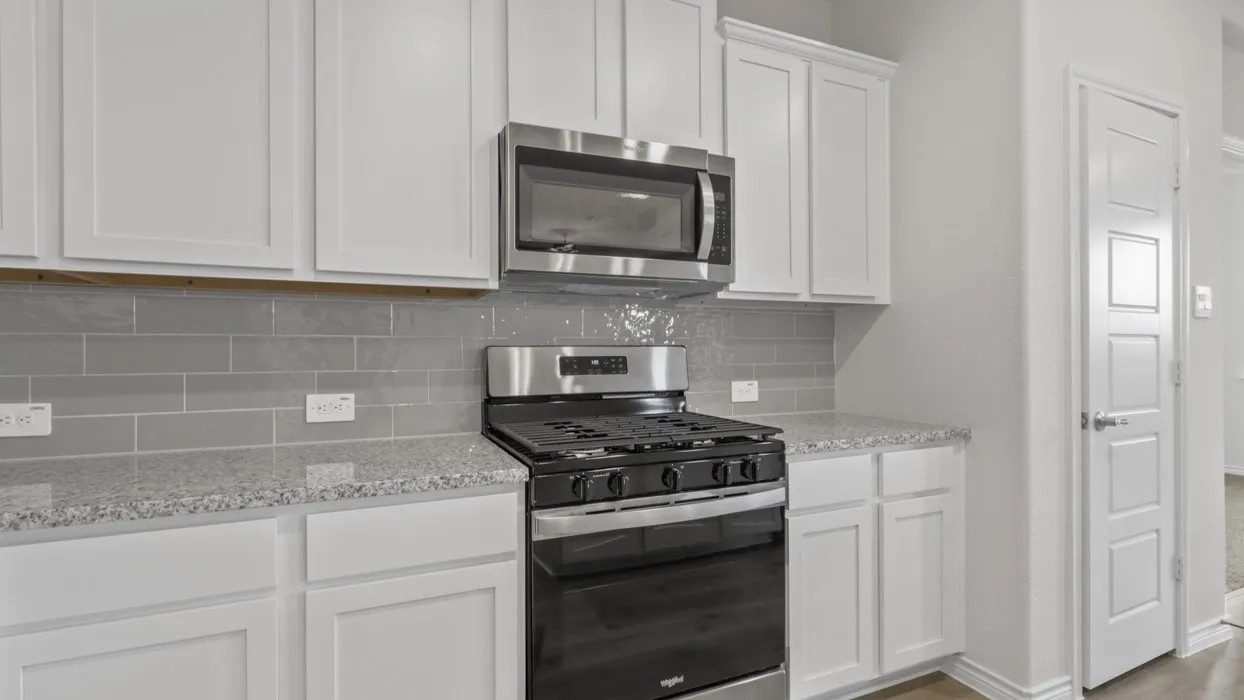 Kitchen with stainless steel appliances, white cabinetry, light stone countertops, and decorative backsplash
