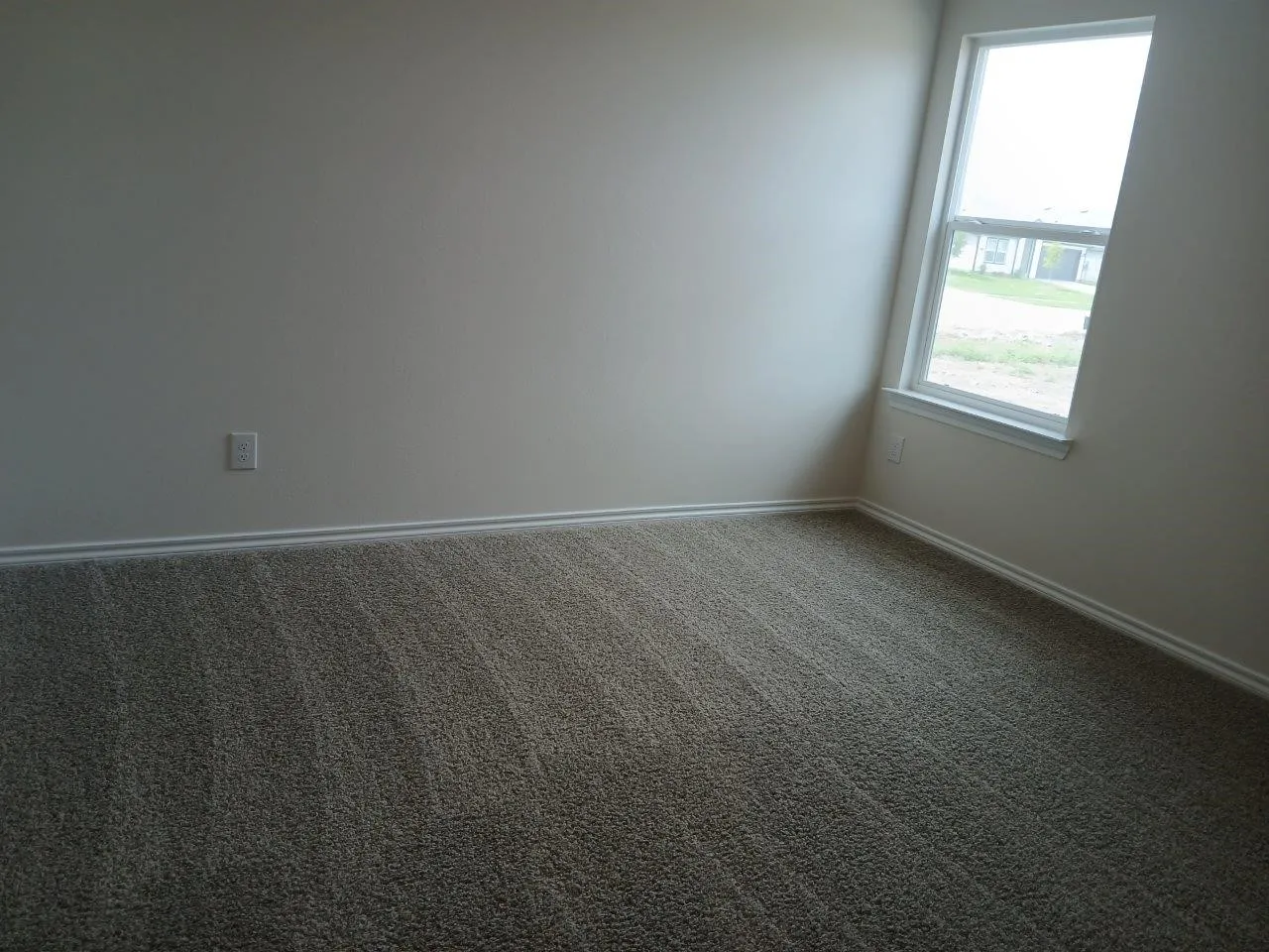 Neutral wall finish with white trim, a single window, and textured carpet flooring