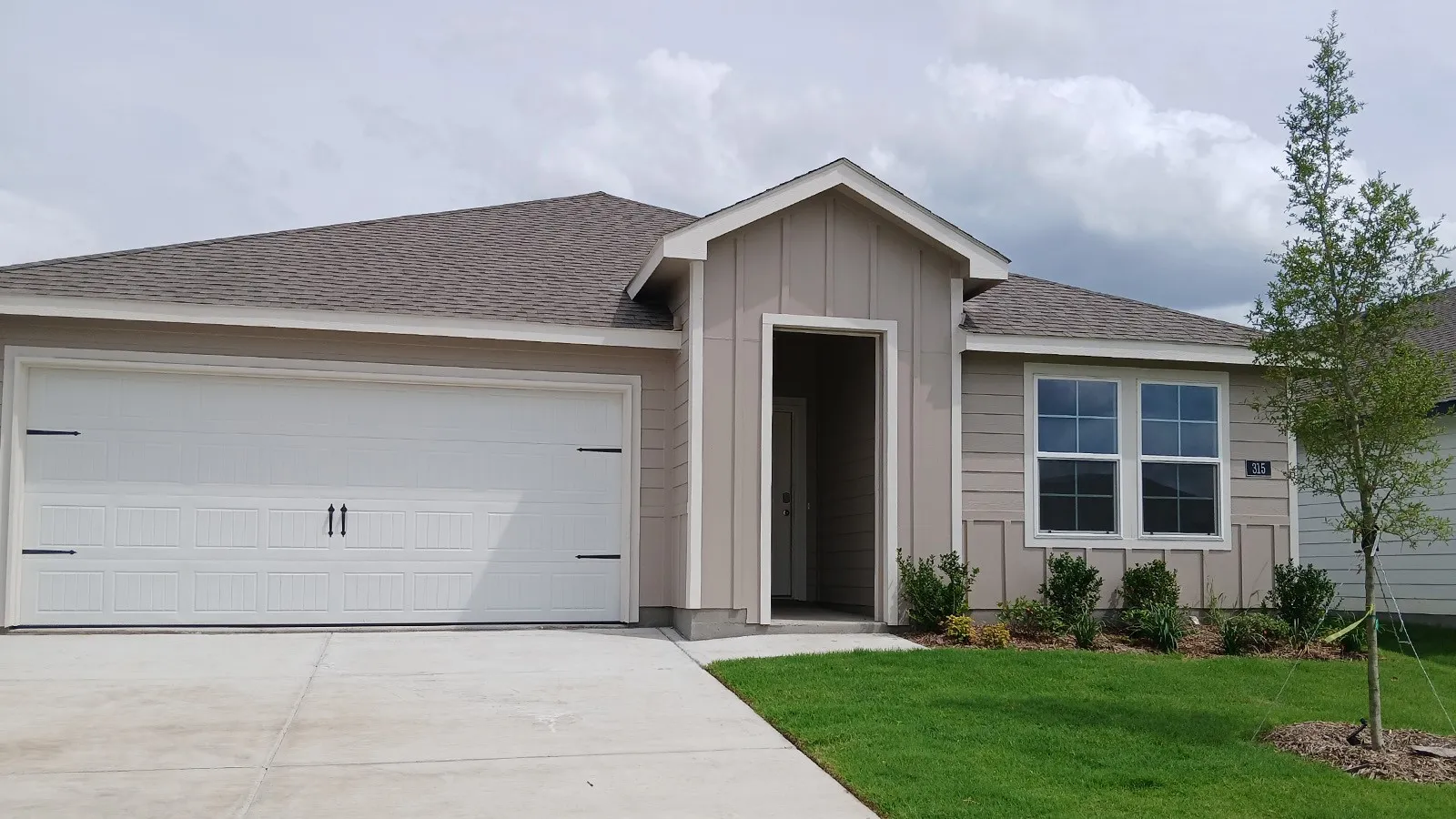 Contemporary single-story residence featuring a two-car garage, beige siding with vertical accents, and a covered entry