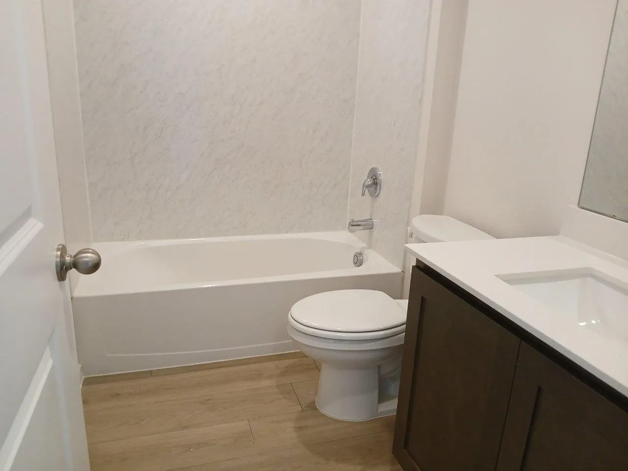 Full bathroom featuring a white tub with integrated shower, white toilet, wood-finish flooring, a dark wood-finish vanity, and a white countertop with an integrated sink