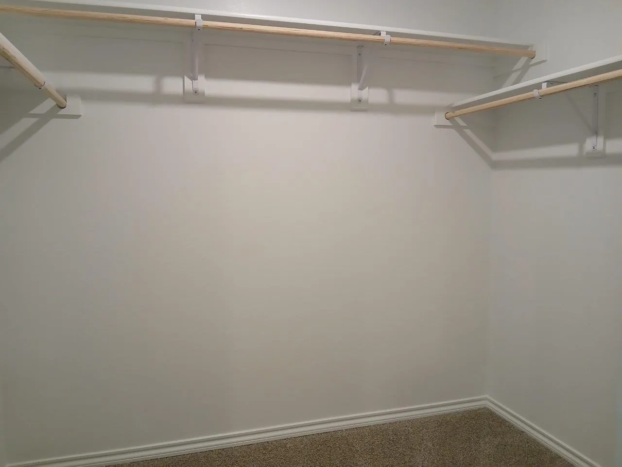 Spacious closet featuring multiple wood closet rods on white shelving brackets, light-colored carpeting, and white baseboard trim