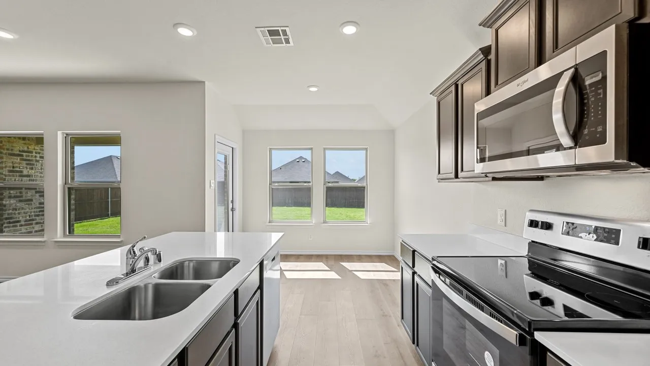 Kitchen with stainless steel appliances, light wood-style flooring, dark wood finish cabinets, light stone counters, and recessed lighting