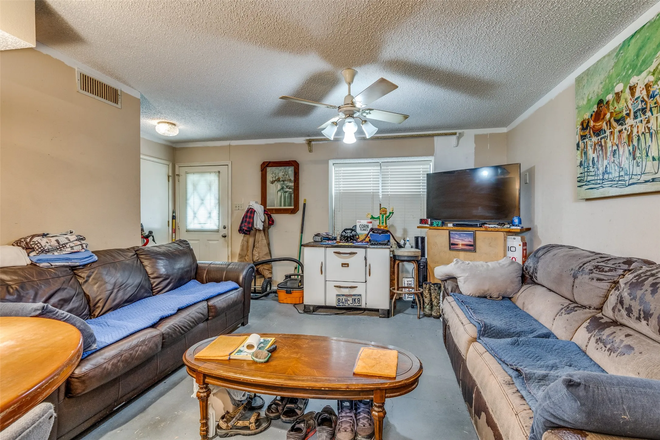 Living room with concrete flooring, a textured ceiling, a ceiling fan, and crown molding