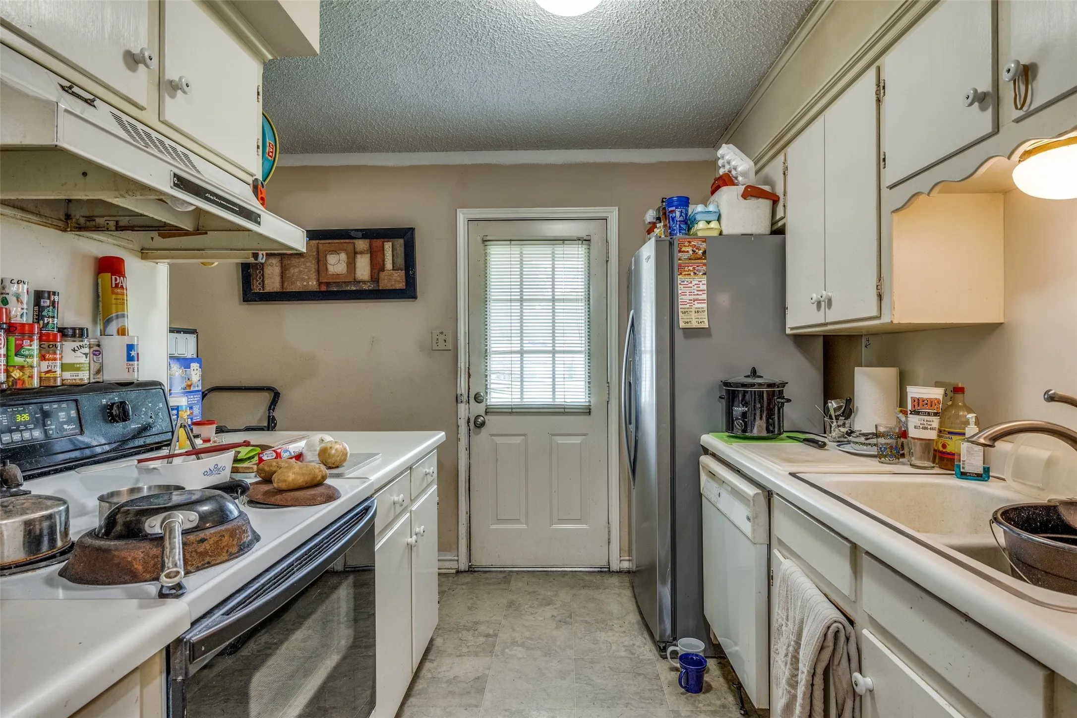 Kitchen with electric range, under cabinet range hood, white dishwasher, light countertops, and a textured ceiling