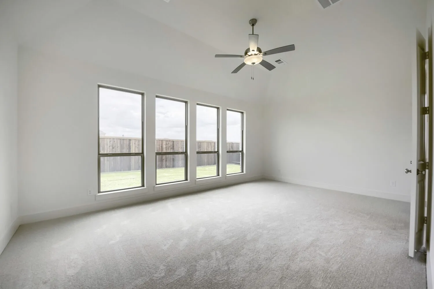 Spacious room featuring vaulted ceilings, a contemporary ceiling fan with integrated lighting, and plush grey carpeting