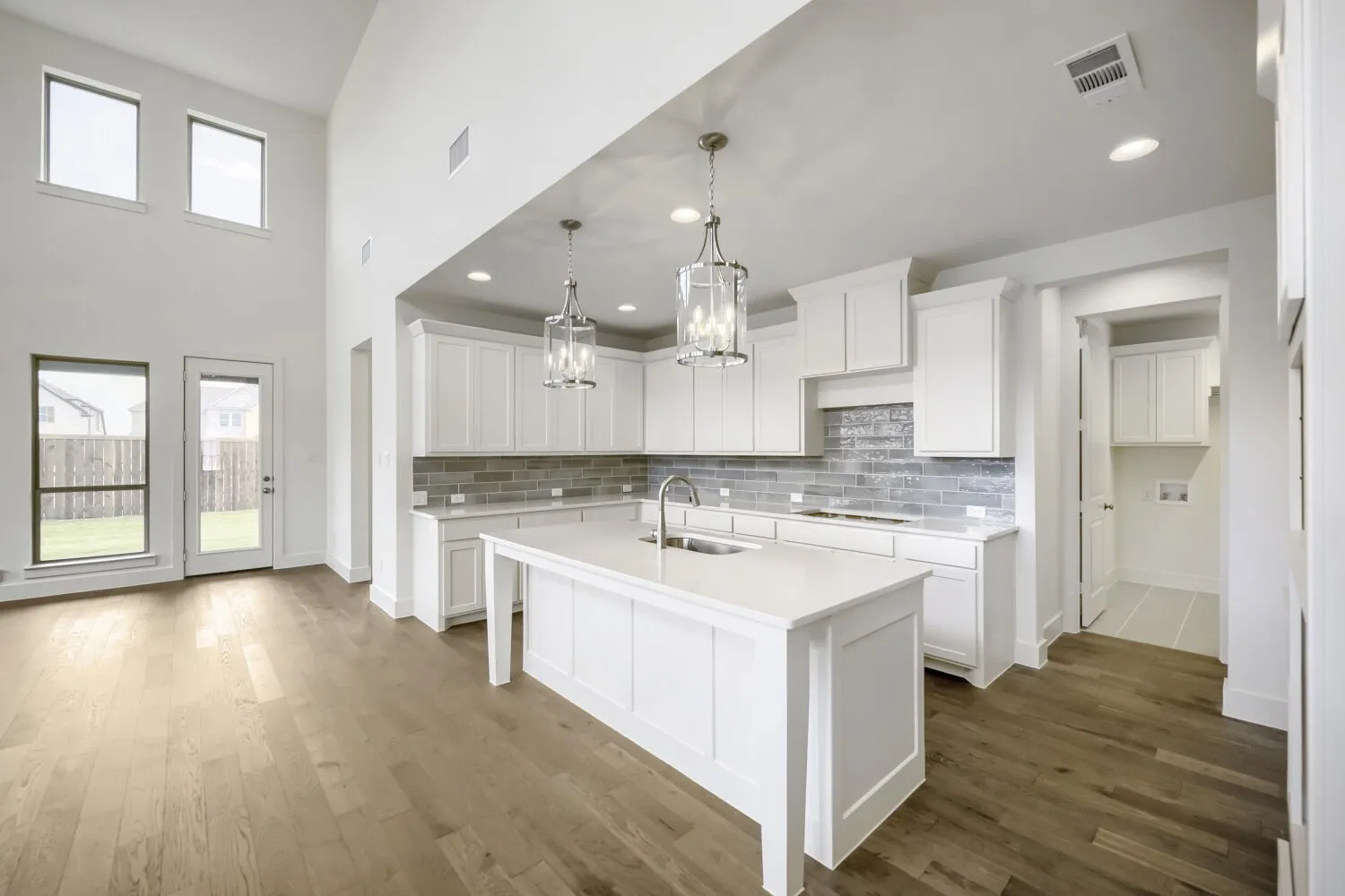 Contemporary kitchen featuring white cabinetry, a large center island with a sink, quartz-finish countertops, and a gray subway tile backsplash