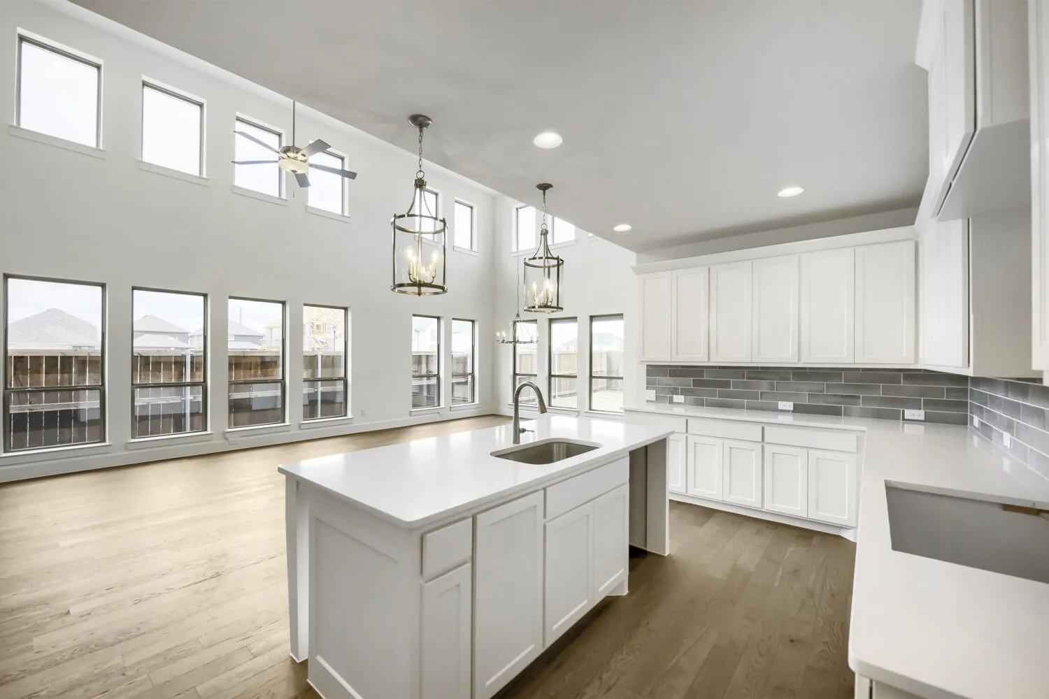 Modern kitchen featuring a central island with an undermount sink, white shaker cabinetry, light-toned countertops, and a gray subway tile backsplash